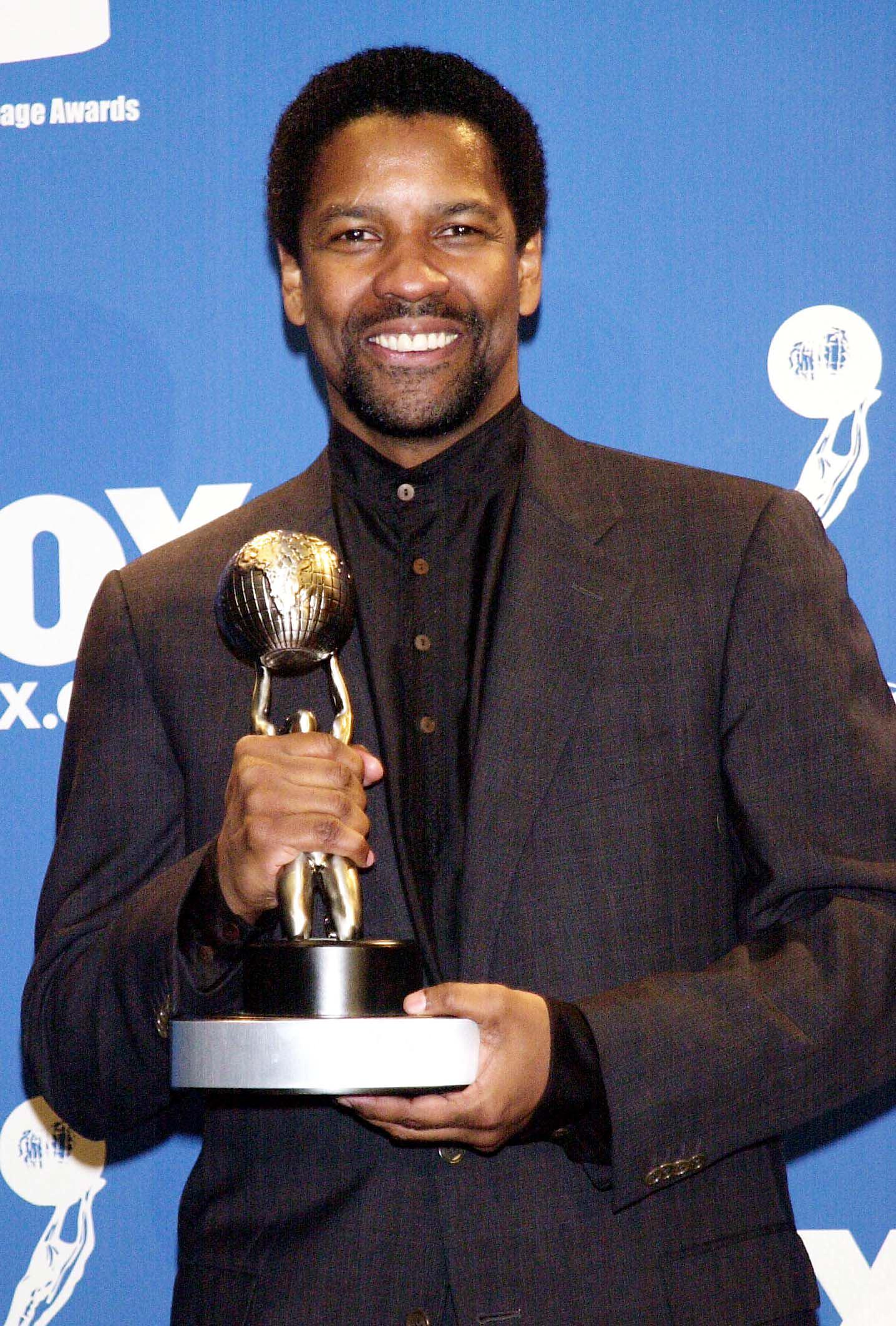 Denzel Washington smiles while holding his NAACP Image Award for "The Hurricane." His defined goatee and mid-length haircut present a matured, polished version of the actor as he enters a new phase of acclaim.