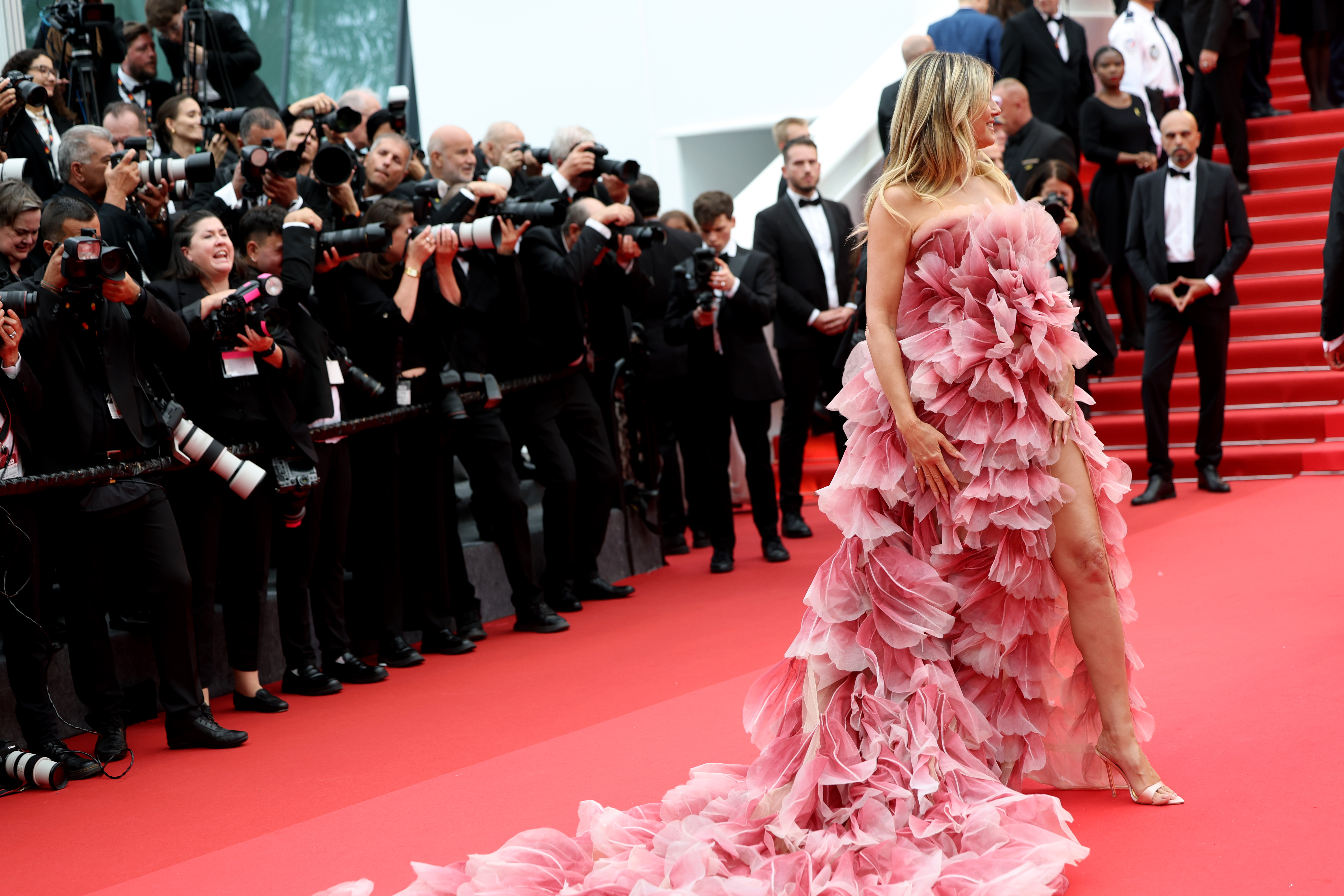 A closer shot reveals the intricate beauty of Klum’s gown—each ruffled layer mimicking delicate petals, softly glowing in shades of pink. The craftsmanship is exquisite, giving the dress a romantic, almost ethereal quality up close.