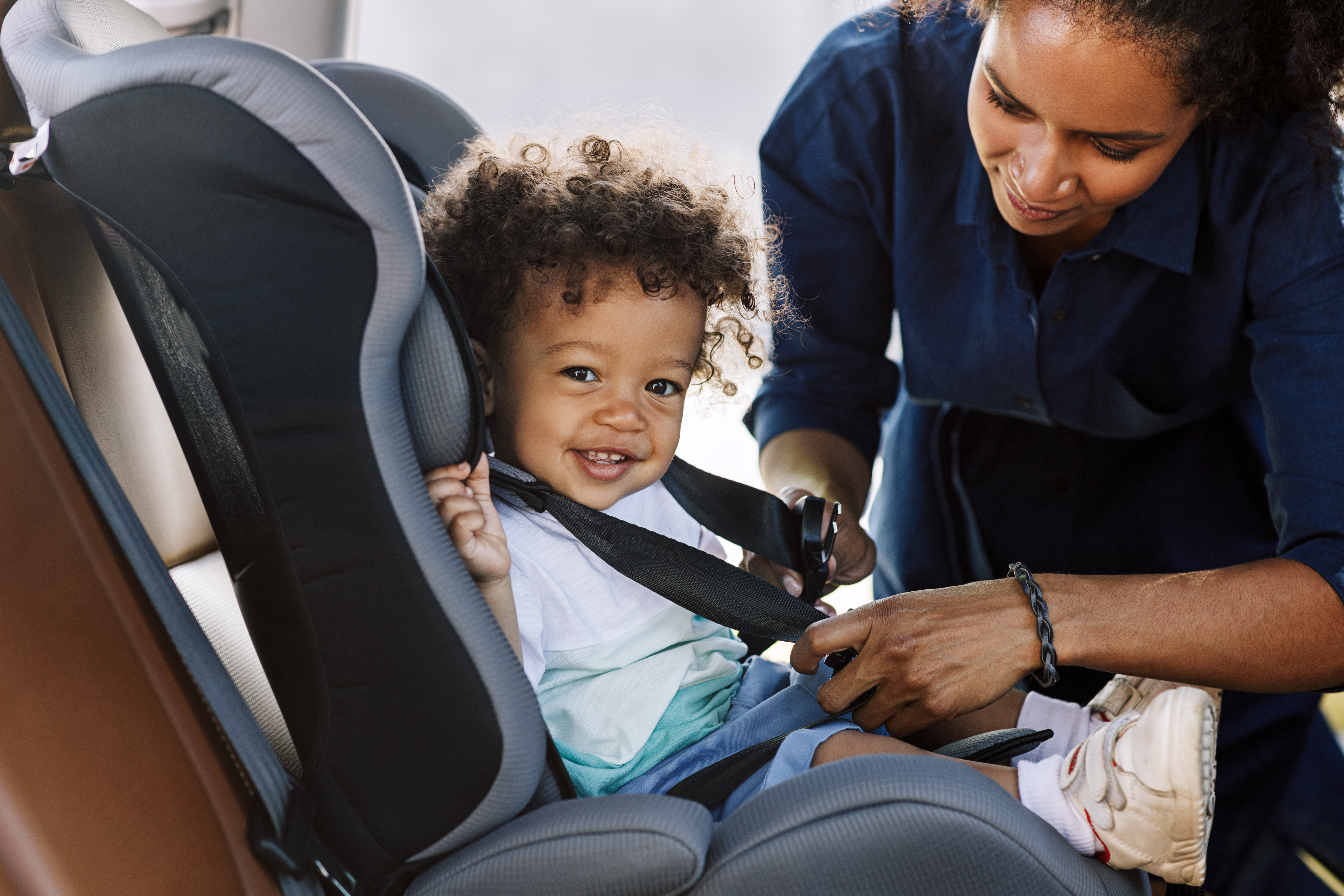 Mother strapping her child to a car seat | Source: Shutterstock