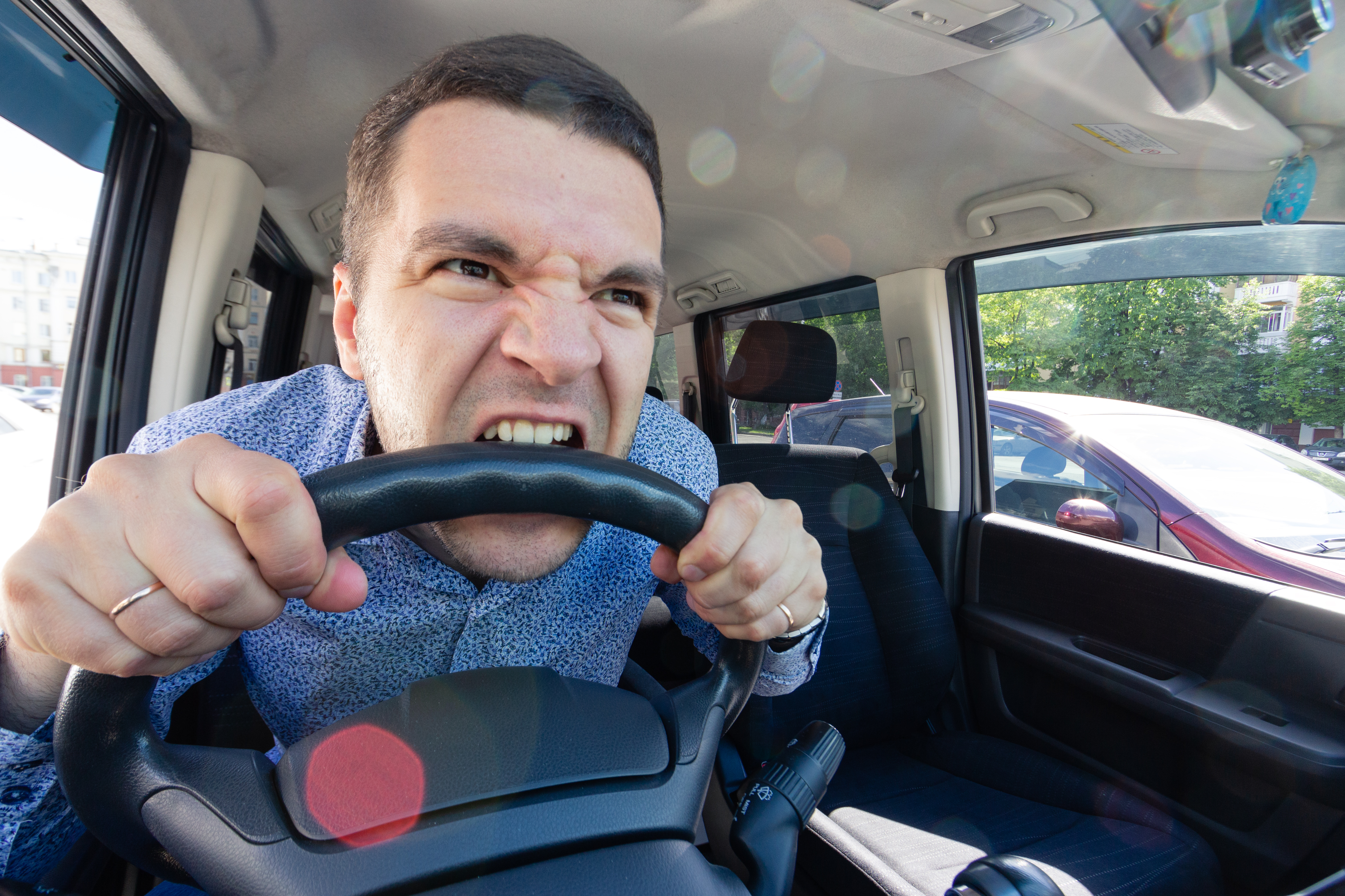 An angry young man bites the wheel of a car | Source: Shutterstock