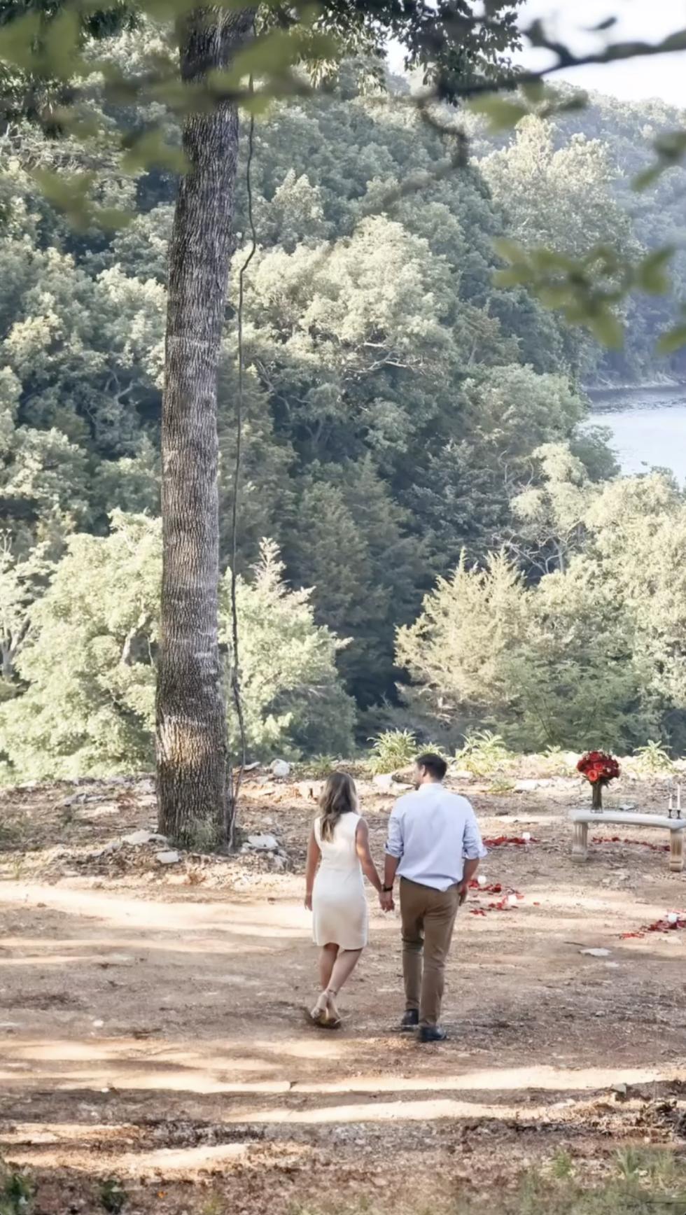 Jana Duggar and Stephen Wissmann walk hand in hand along a wooded path, framed by tall trees and overlooking the water, as they approach a romantic setup ahead. | Source: Instagram/janamduggar
