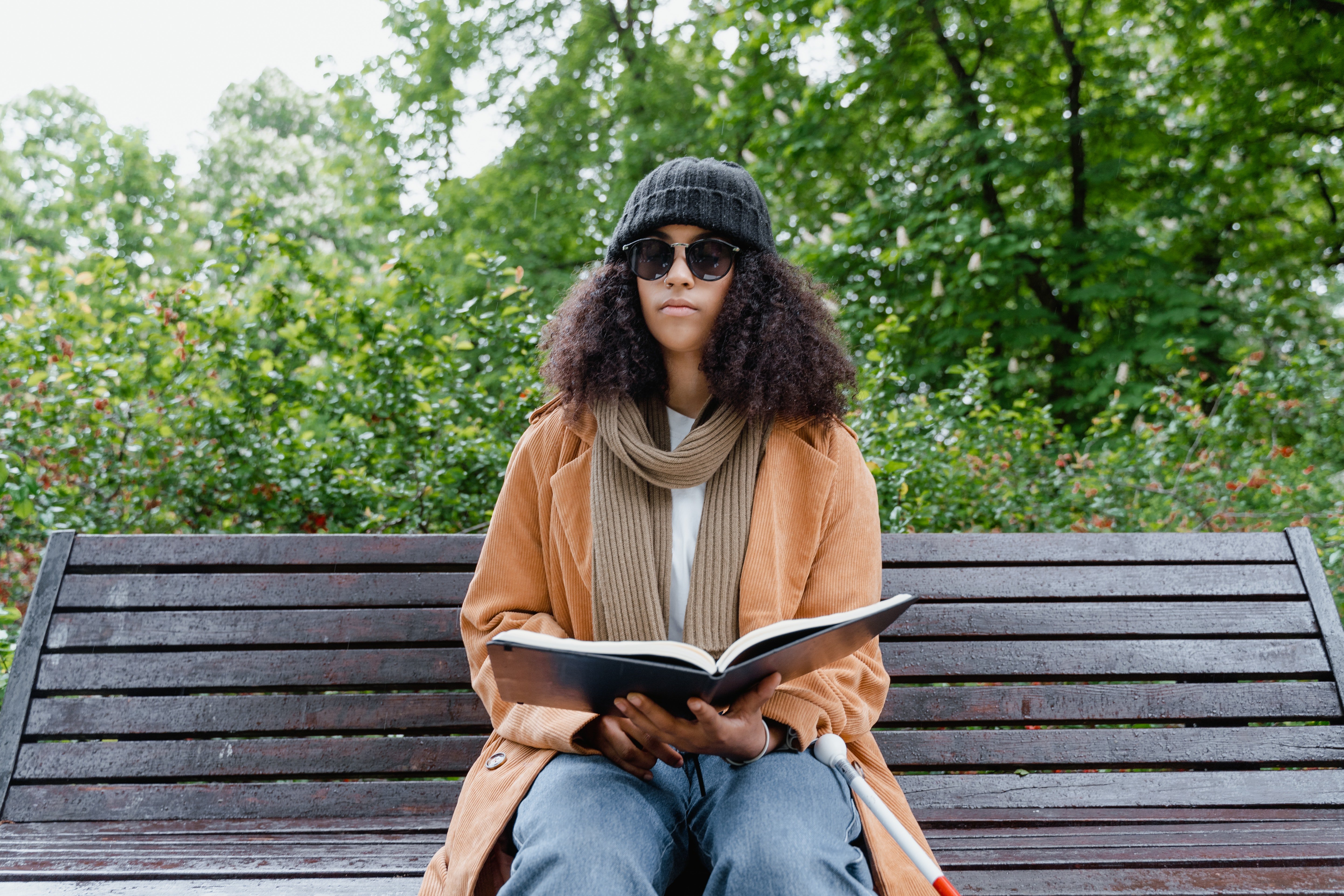 Pictured - A young woman sitting on a bench holding a book wearing sunglasses | Source: Pexels 