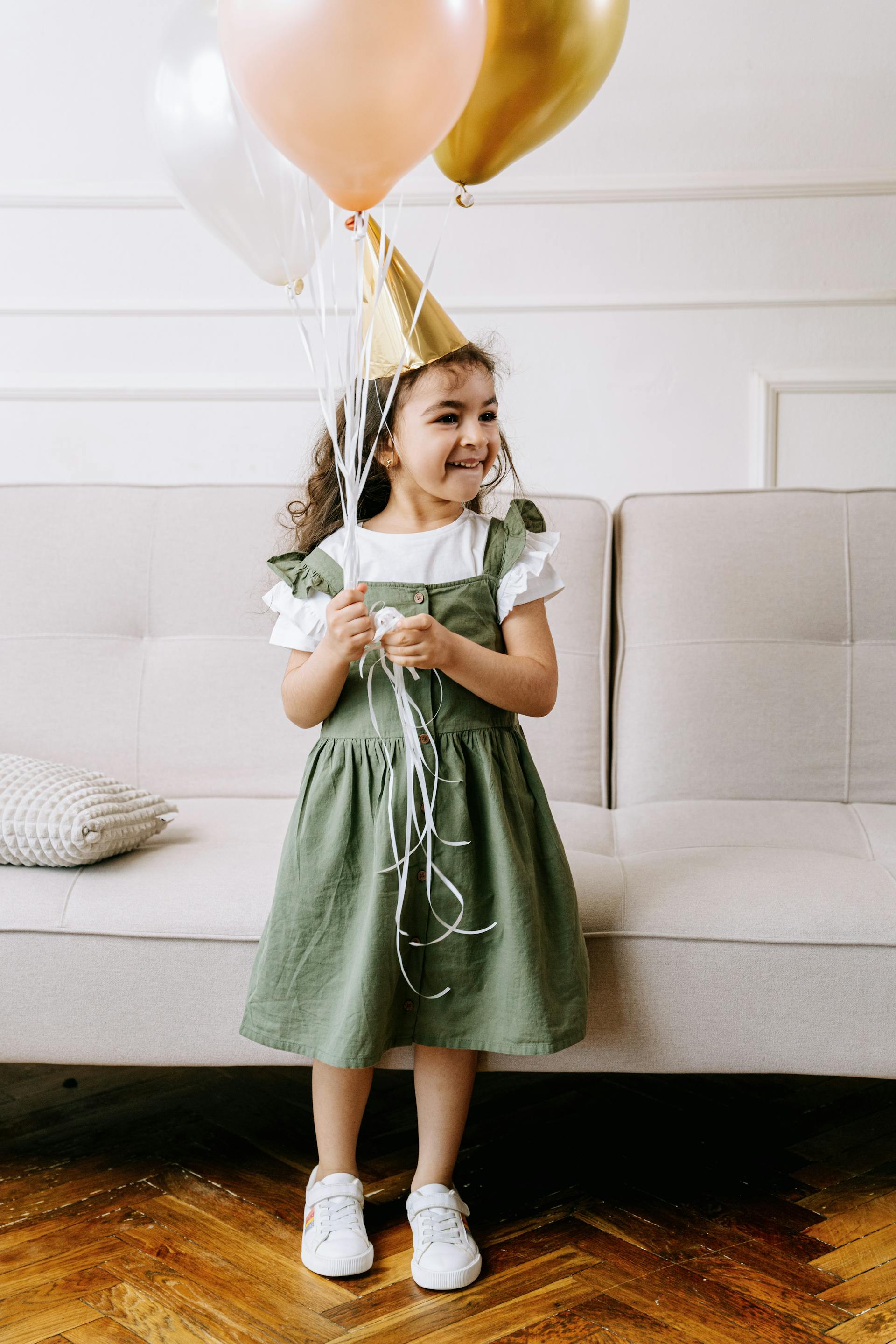 A little girl wearing a party hat while holding balloons | Source: Pexels