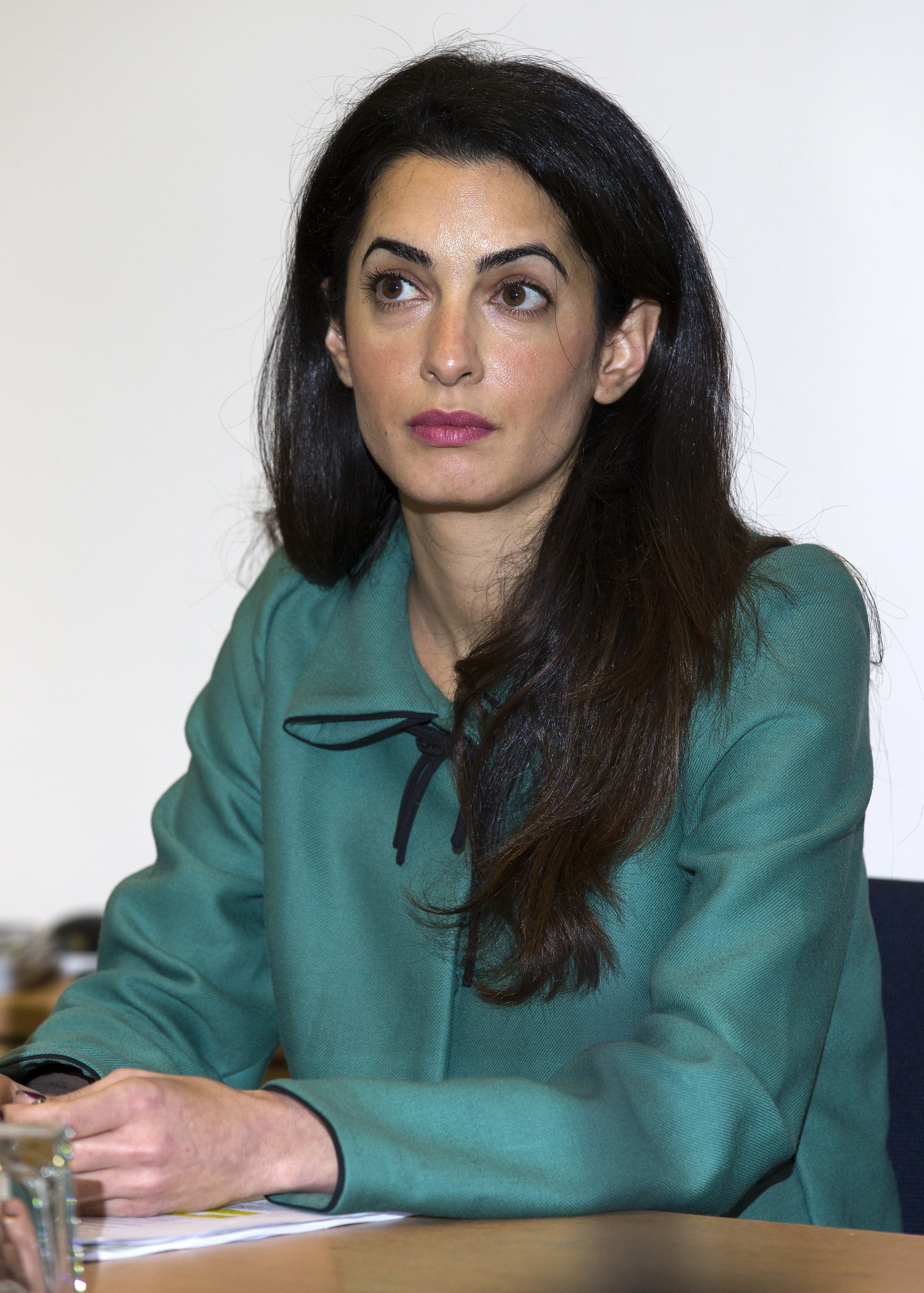 Amal is seen at a London press conference wearing a sea-green tailored jacket with a black ribbon tie at the collar. Her long, dark hair is worn loose, cascading softly over her shoulders in an early glimpse of her signature elegance.