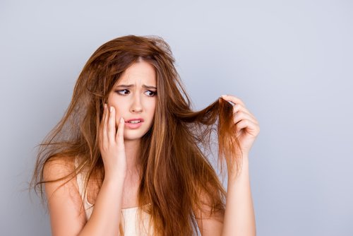 Frau betrachtet schockiert ihre kaputten Haare | Quelle: Shutterstock