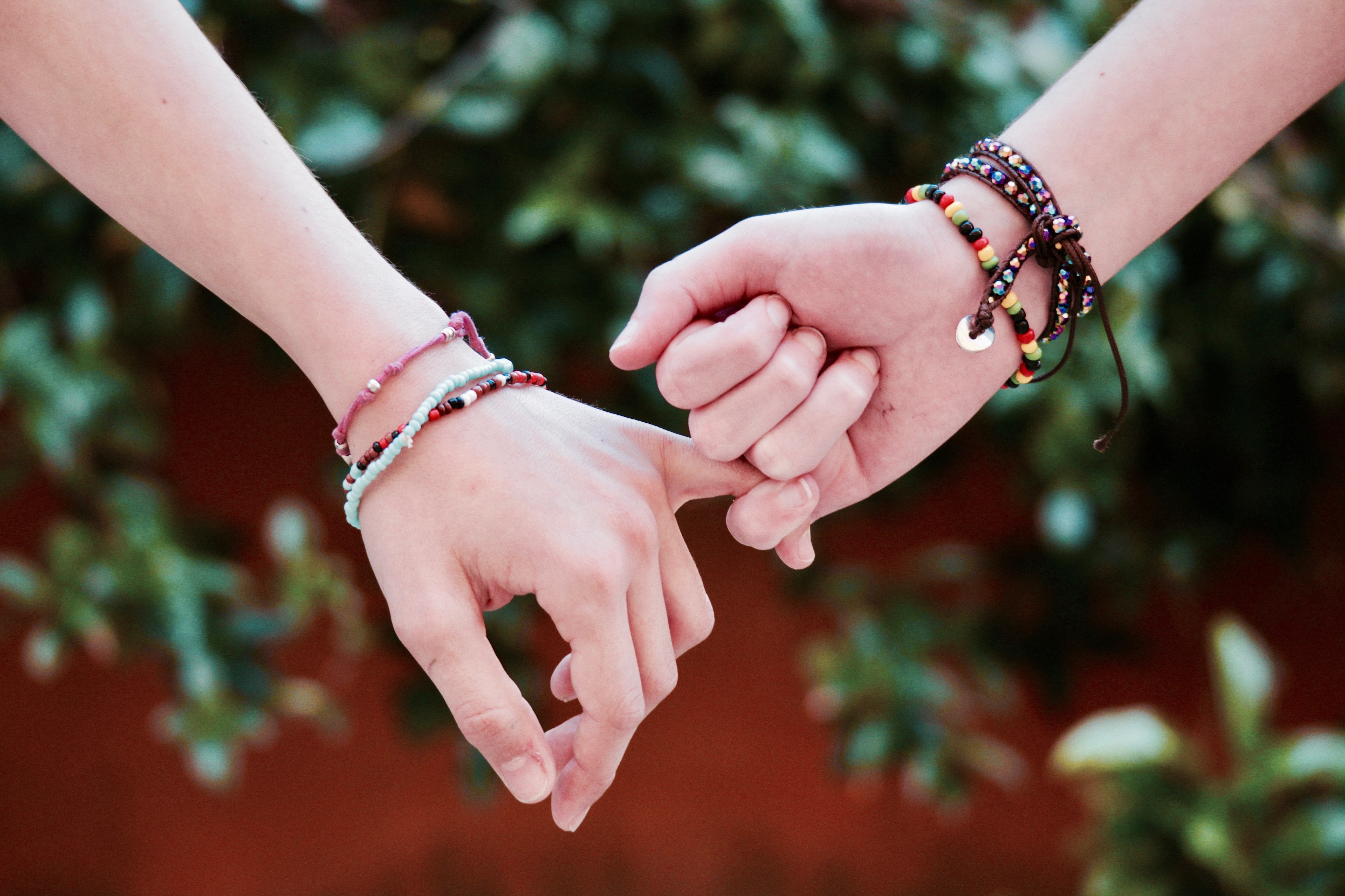 Two individuals holding each others' pinkies with friendship bracelets on. | Source: Pexels