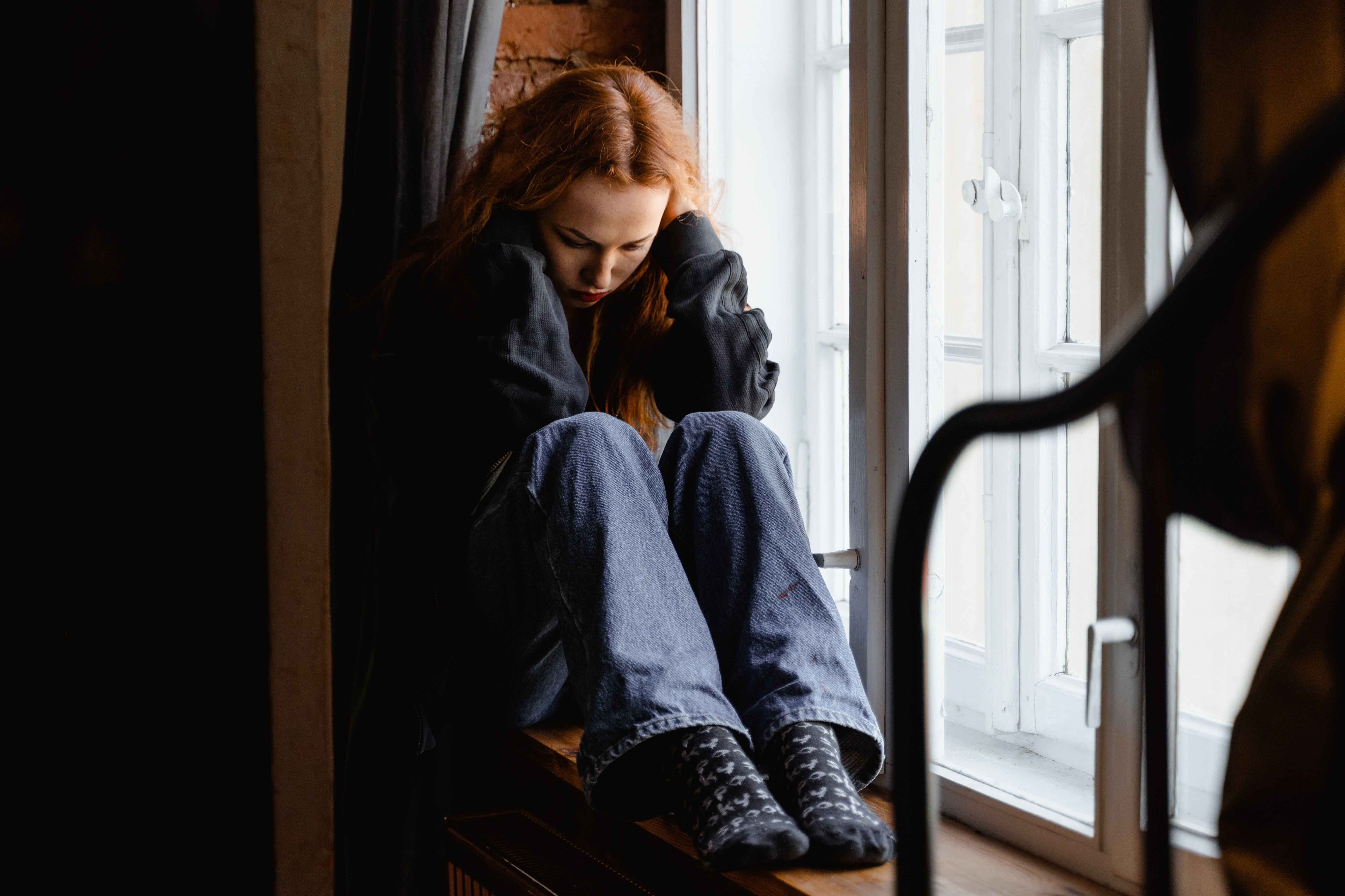 An upset young woman sitting curled up in a corner with her hands around her head | Source: Pexels