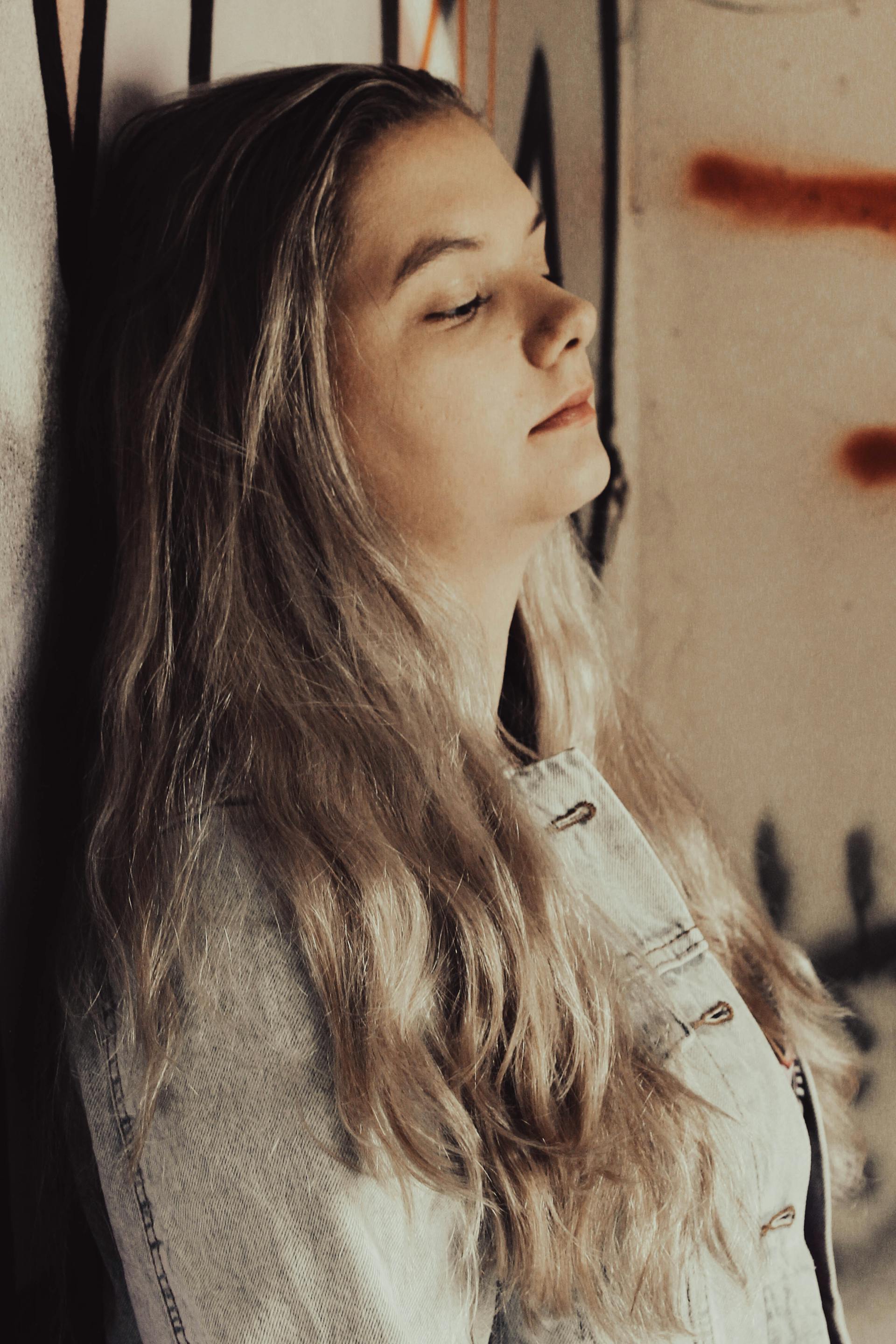 Una mujer triste con una chaqueta vaquera y los ojos cerrados, apoyada contra una pared | Fuente: Pexels