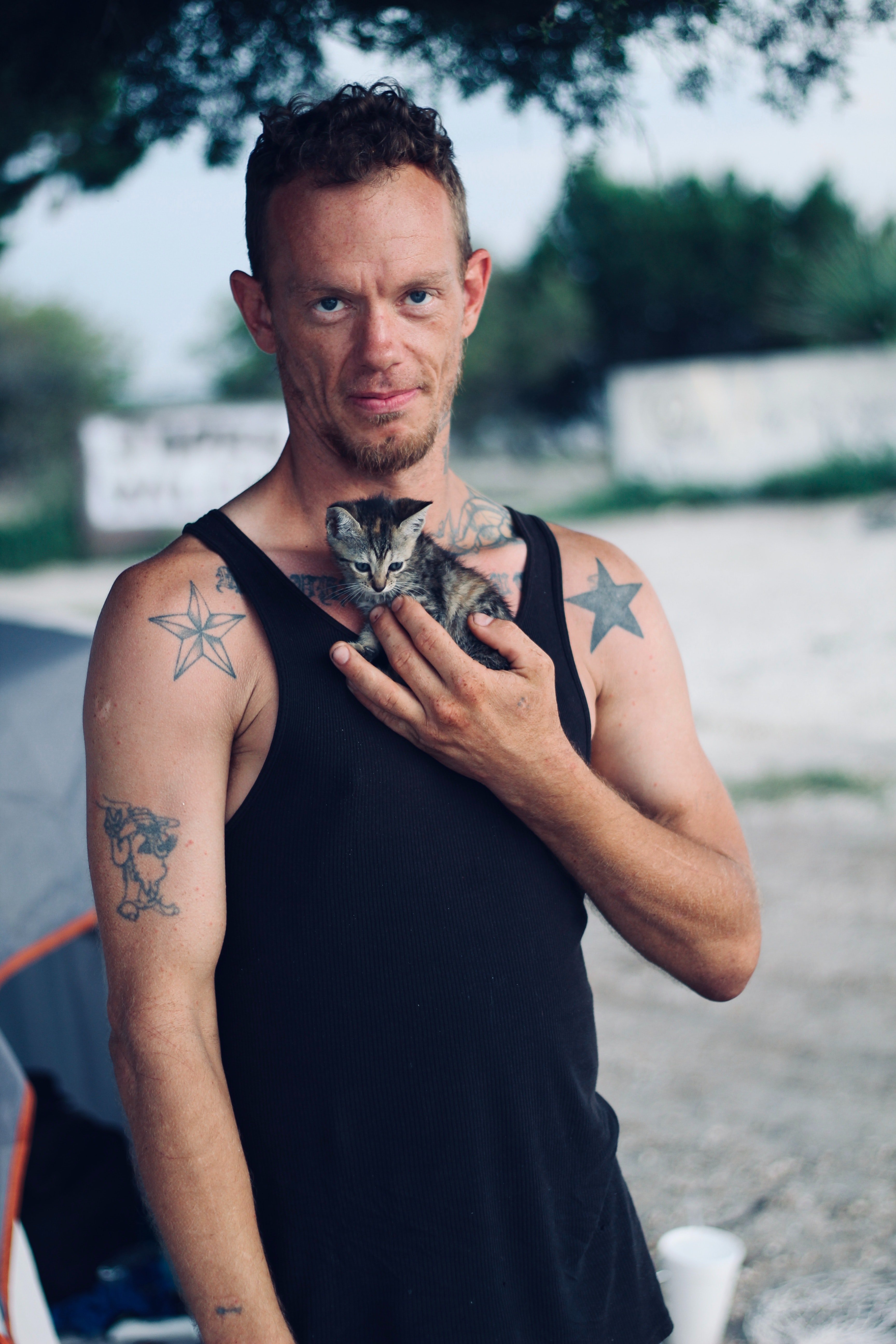 Pictured - A man wearing a black tank top with visible tattoos carrying a brown tabby cat | Source: Pexels 