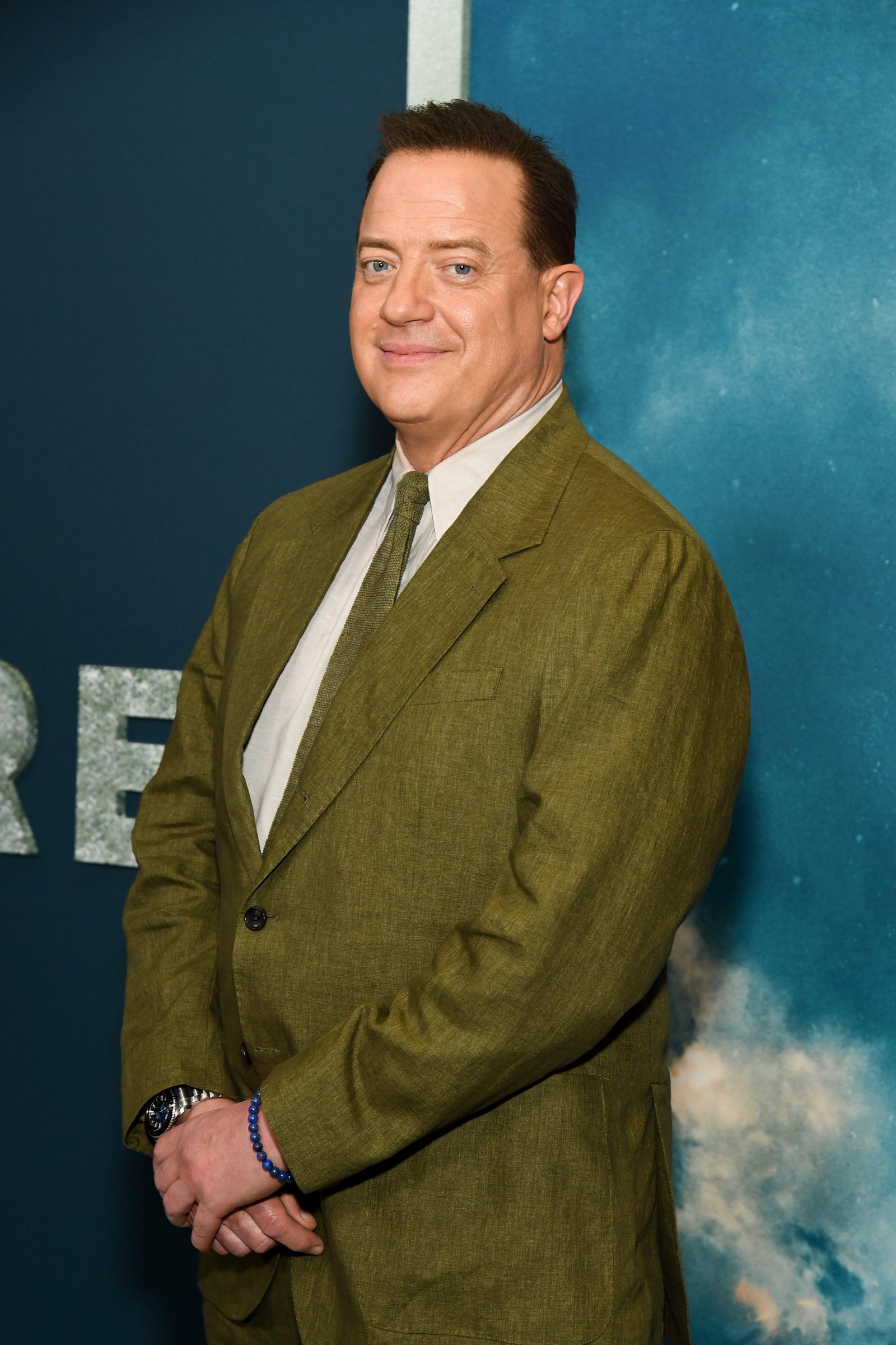 Brendan Fraser stands with his hands clasped, wearing an olive suit and matching tie at the New York premiere of "Pressure," held at AMC Lincoln Square 13.
