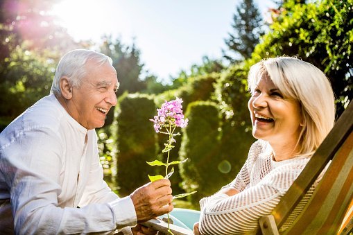 Photo of a happy senior man presenting flower to his wife in a garden | Photo: Getty Images