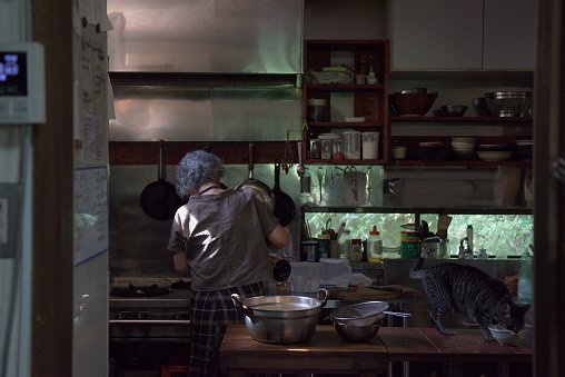 Photo of an old woman cooking in a kitchen and cat | Photo: Getty Images