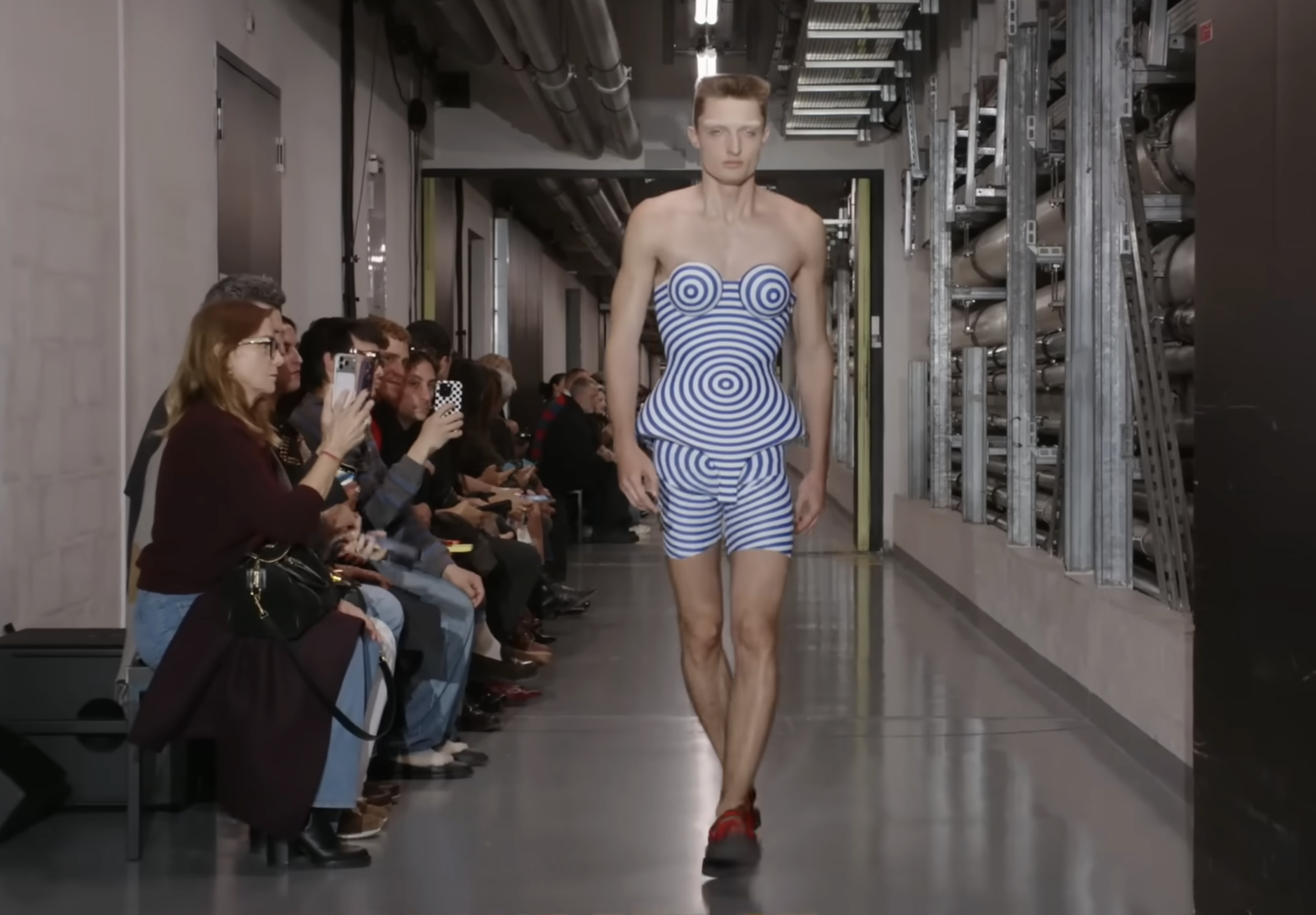 A model showcases another futuristic design that appears to feature a 3D-printed effect. The peplum-shaped top is paired with matching shorts, creating a daring and modern look on the male model. From a post dated October 5, 2025. Source: Youtube/@jeanpaulgaultier