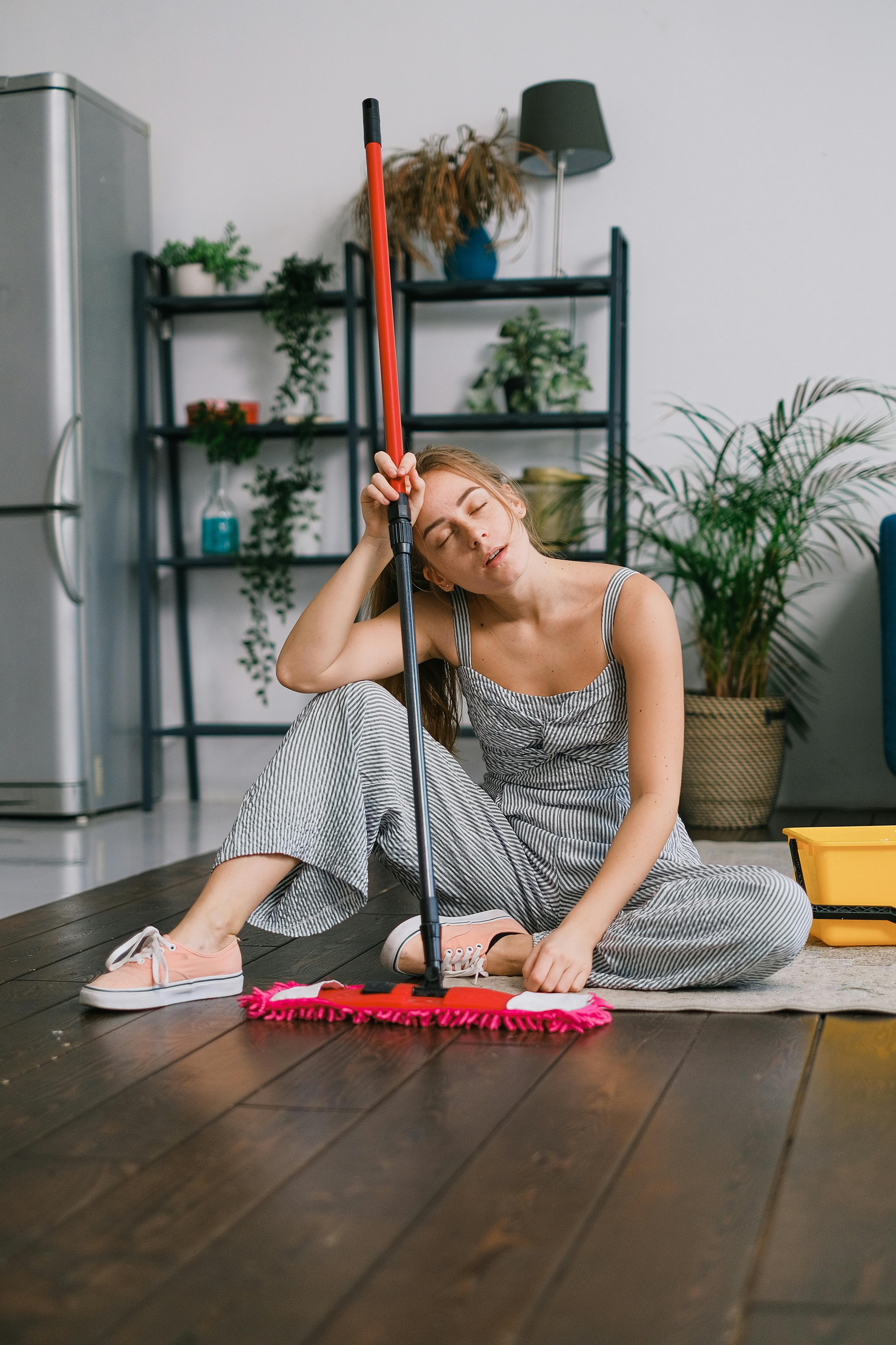Woman on the floow looking tired as she holds a mop | Source: Pexels