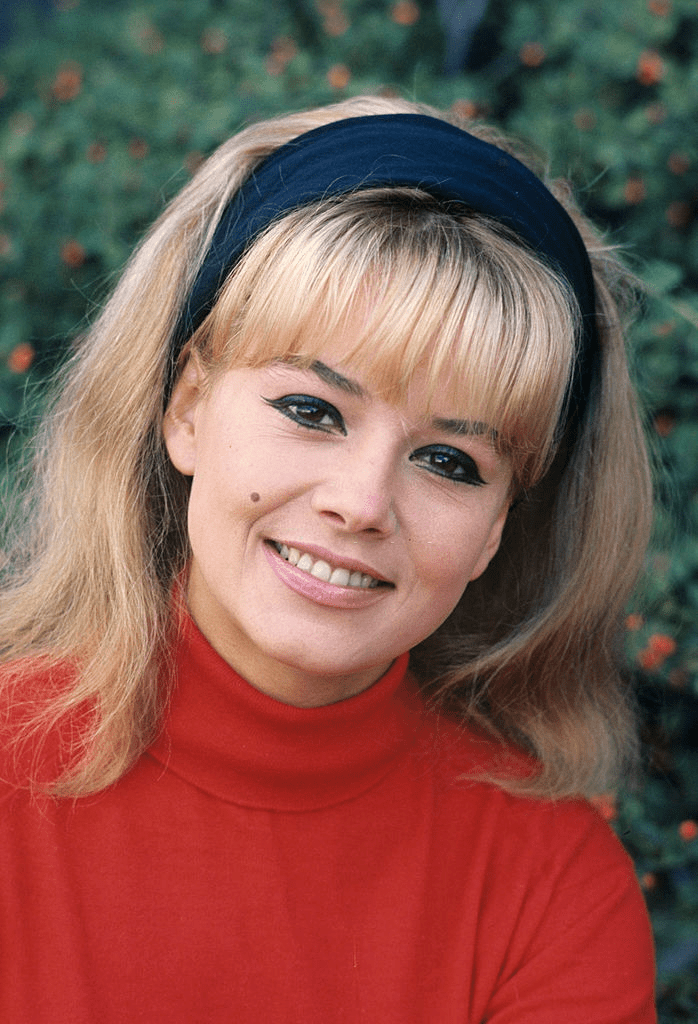 Portrait de Sophie DAUMIER, souriant, vêtue d'un pull à col roulé rouge, un bandeau noir dans ses cheveux blonds en extérieur. | Photo : Getty Images Portrait de Sophie DAUMIER, souriant, vêtue d'un pull à col roulé rouge, un bandeau noir dans ses cheveux blonds en extérieur. | Photo : Getty Images