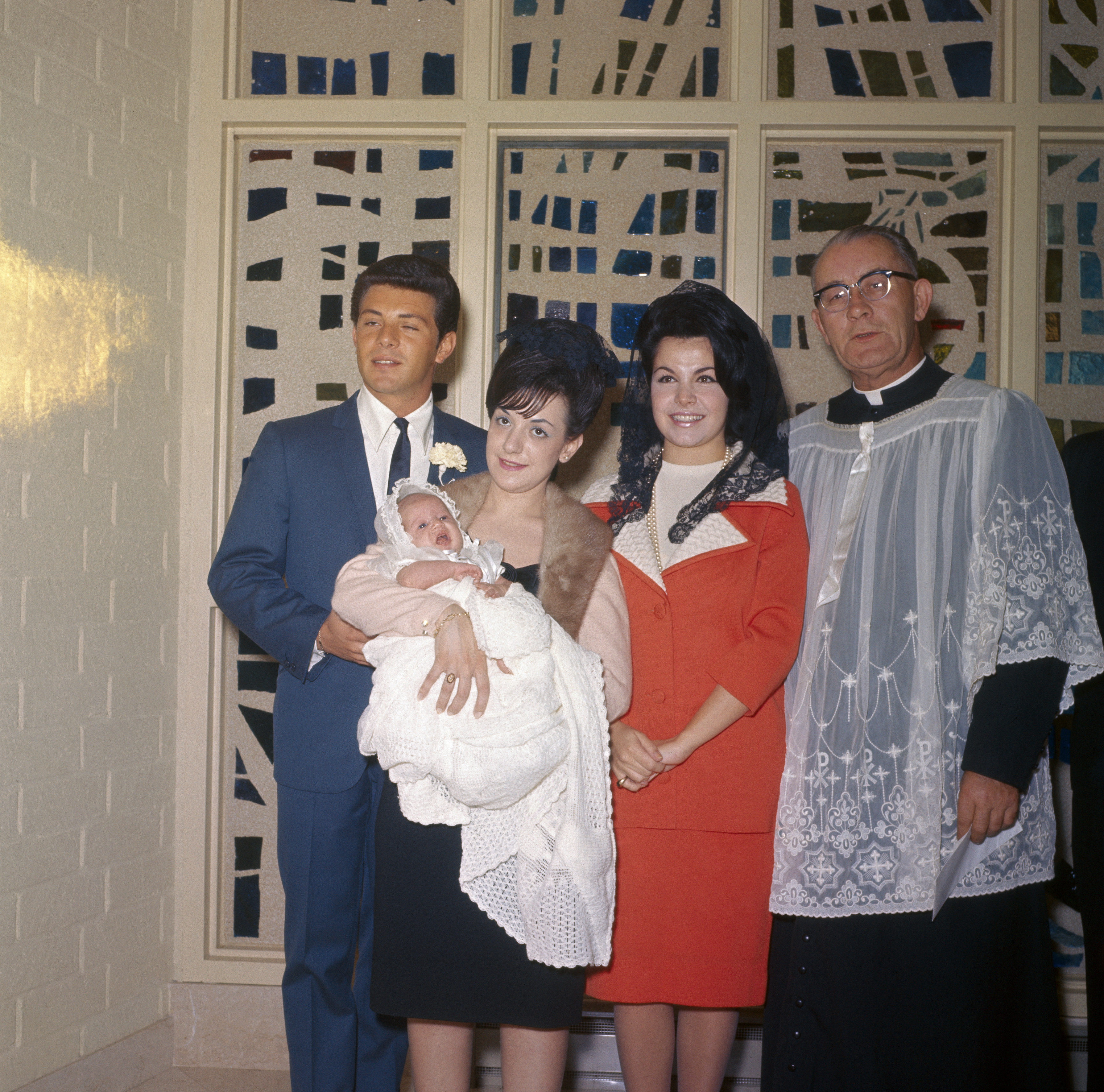 Annette Funicello with daughter Gina, Gina's godparents, Marine Ann Schiochi and Frankie Avalon, and the presiding priest circa 1965. | Source: Getty Images