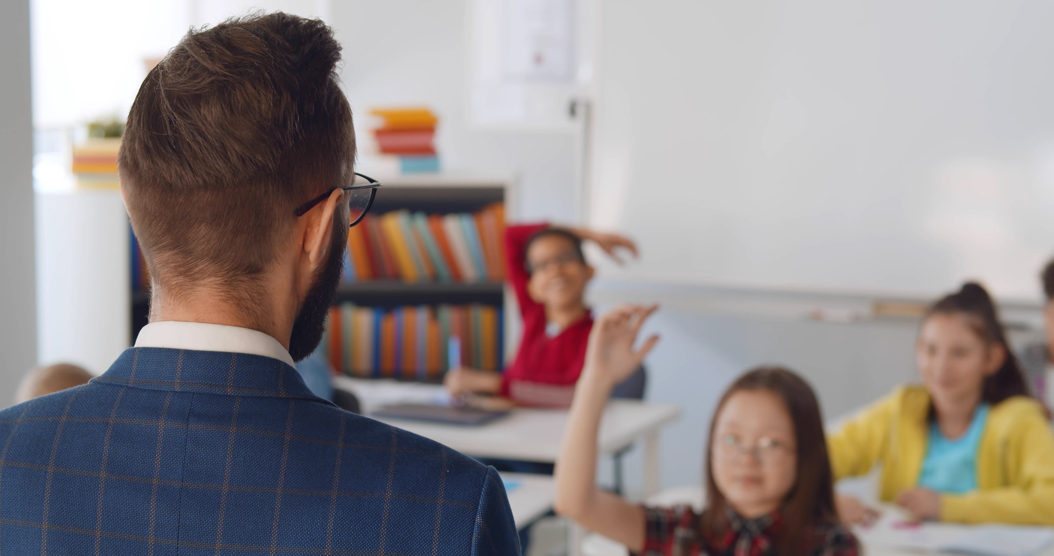 Un professeur de sexe masculin et des écoliers assis à leur bureau en classe. | Photo : Shutterstock