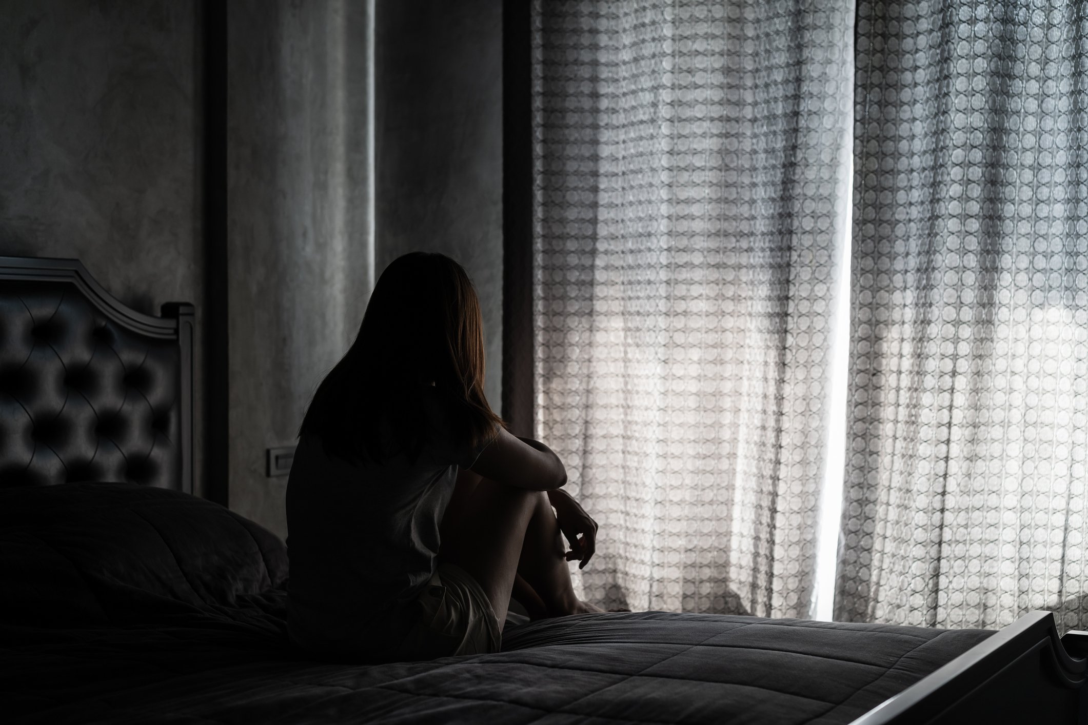 Rückansicht der depressiven Frau, die zu Hause auf dem Bett sitzt I Quelle: Getty Images