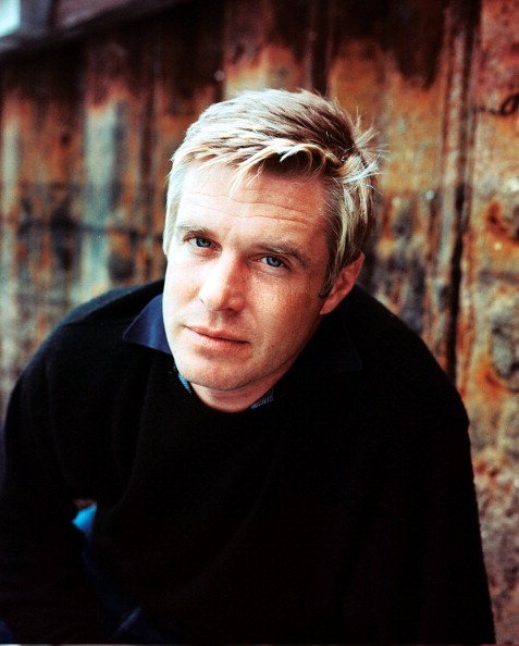 George Peppard wearing a black jumper as he poses against a rusted surface | Photo: Getty Images