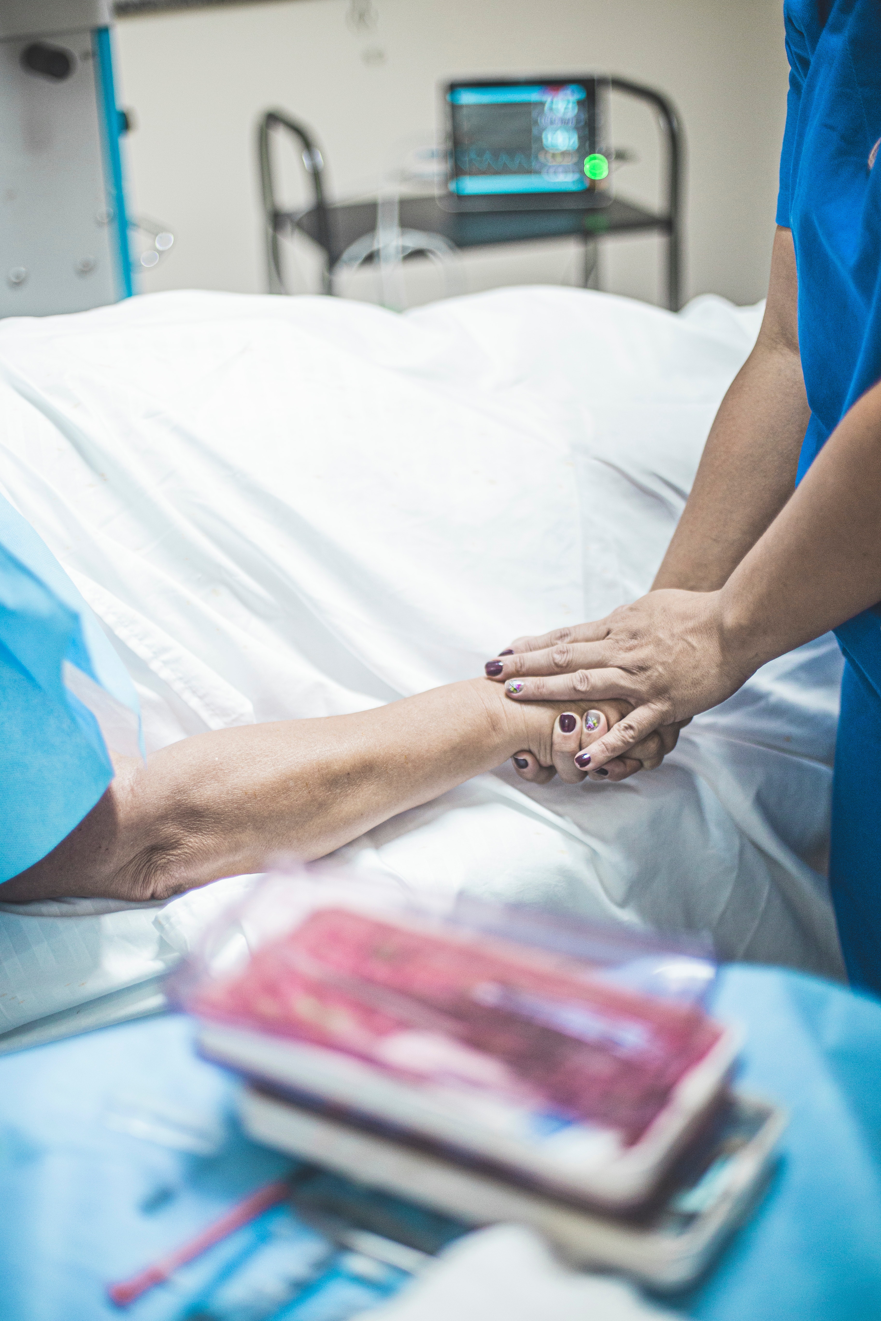 Person in blue scrubs holding the hand of a patient lying on bed | Source: Pexels
