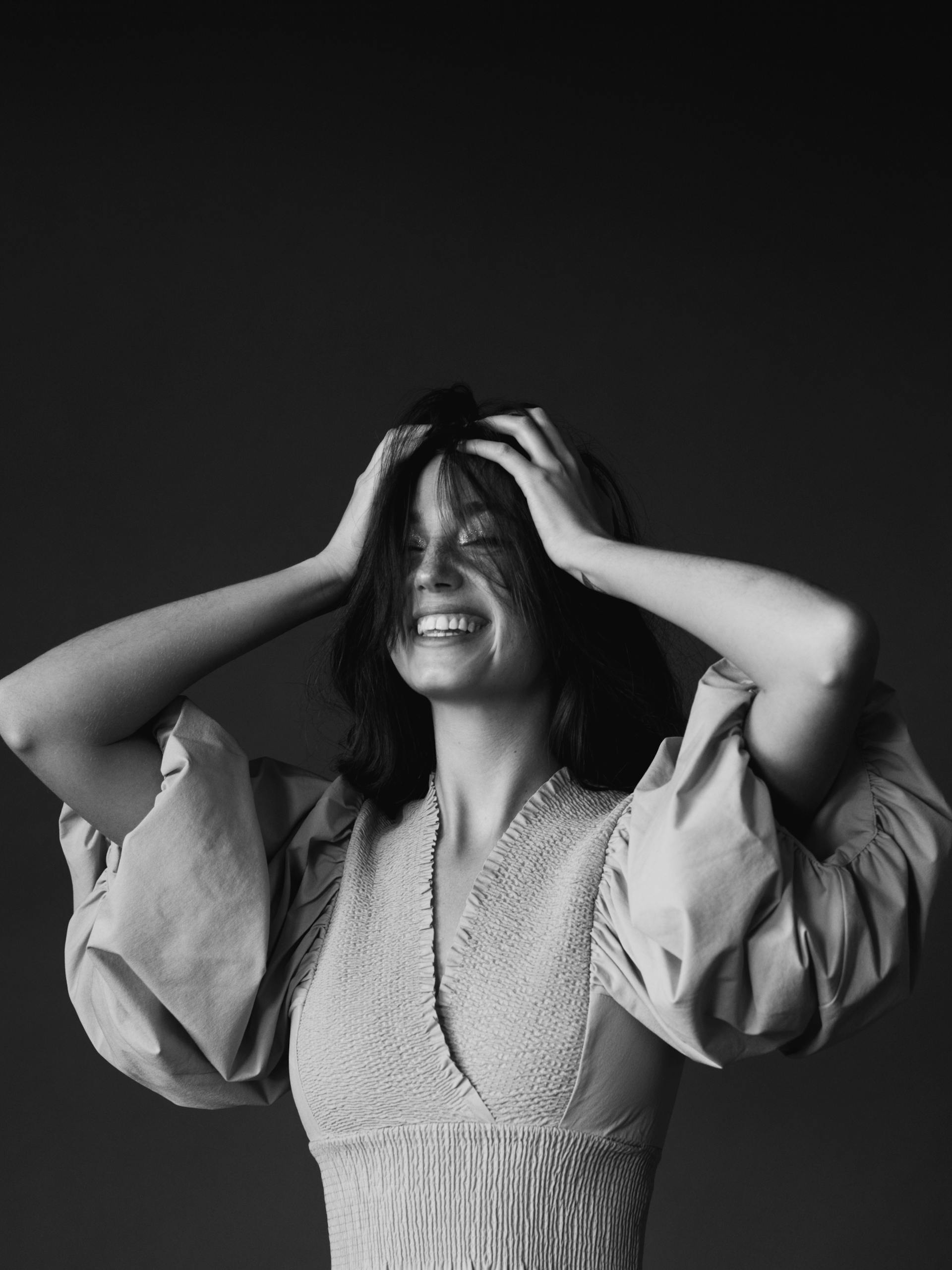 A grayscale photo of a woman laughing while covering her head with both hands | Source: Pexels