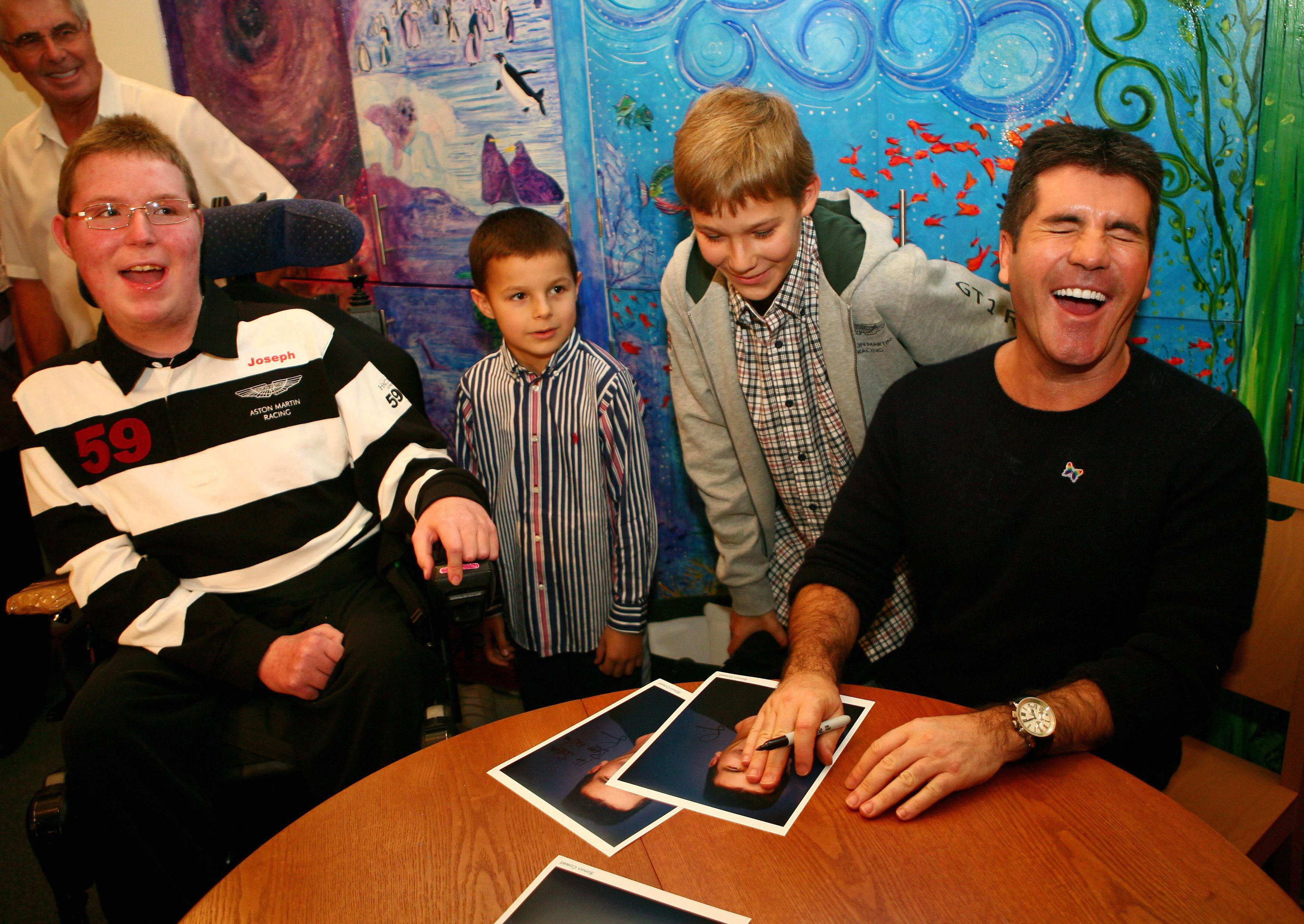 Simon Cowell signs autographs for Joseph, 16, Alex, seven and Mathew Ball, 11, during a visit to Christopher's Children's Hospice in Guildford, Surrey, as he becomes patron of national charity, Children's Hospices UK. | Source: Getty Images 