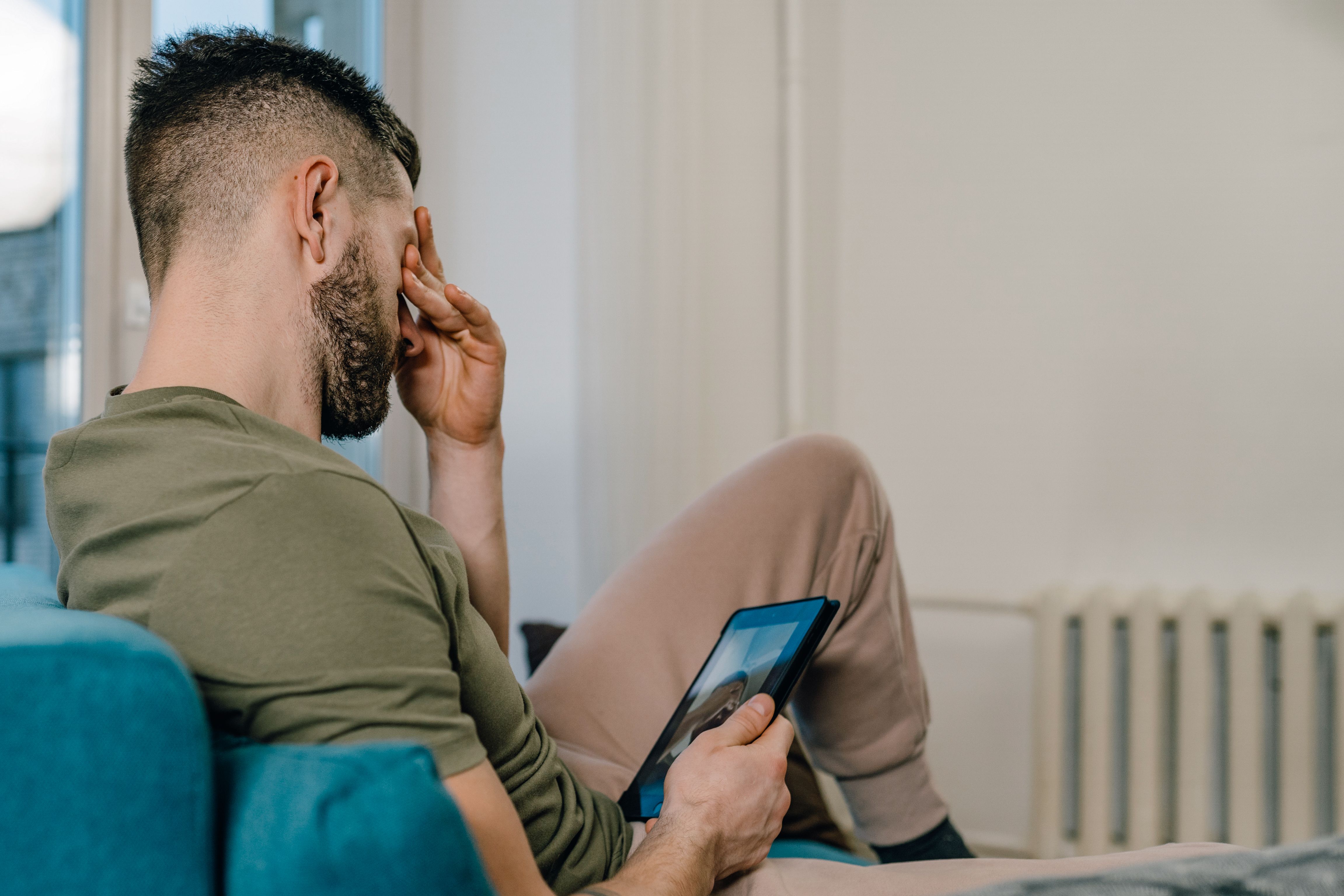 Distressed man sittting on a couch with his phone | Source: Pexels
