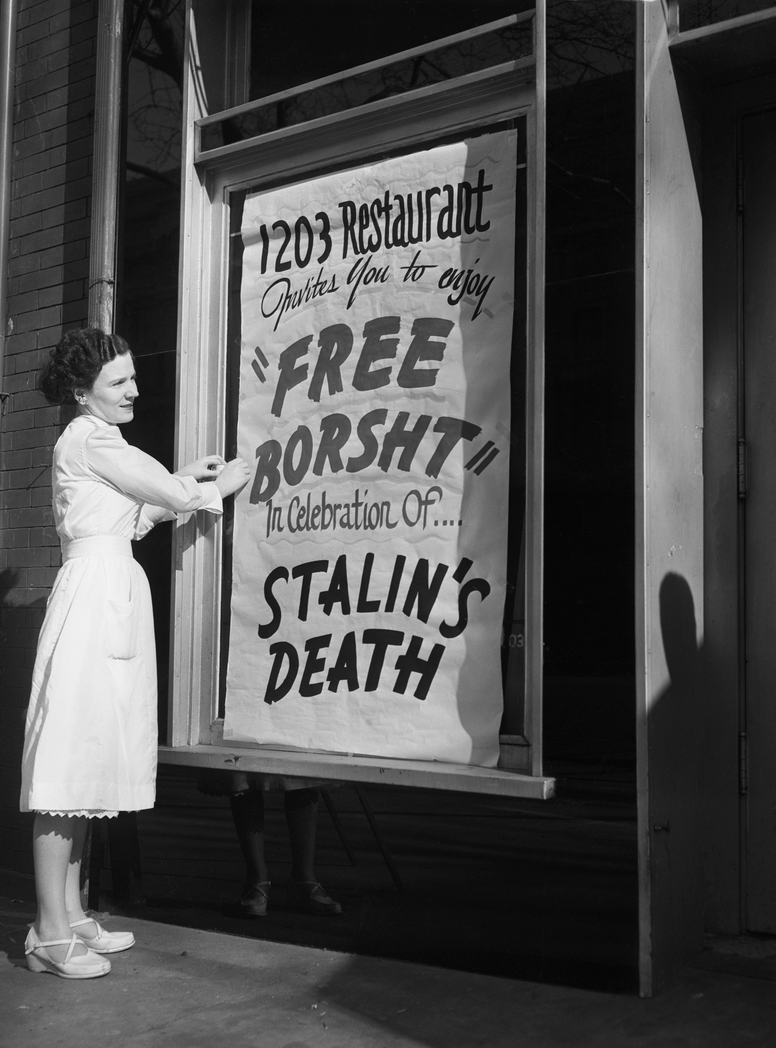 Eileen Keenan, a waitress at the 1203 Restaurant, puts up a sign outside the restaurant on March 6, 1953, inviting everyone to enjoy "Free Borst" in celebration of Stalin's death. | Source: Getty Images