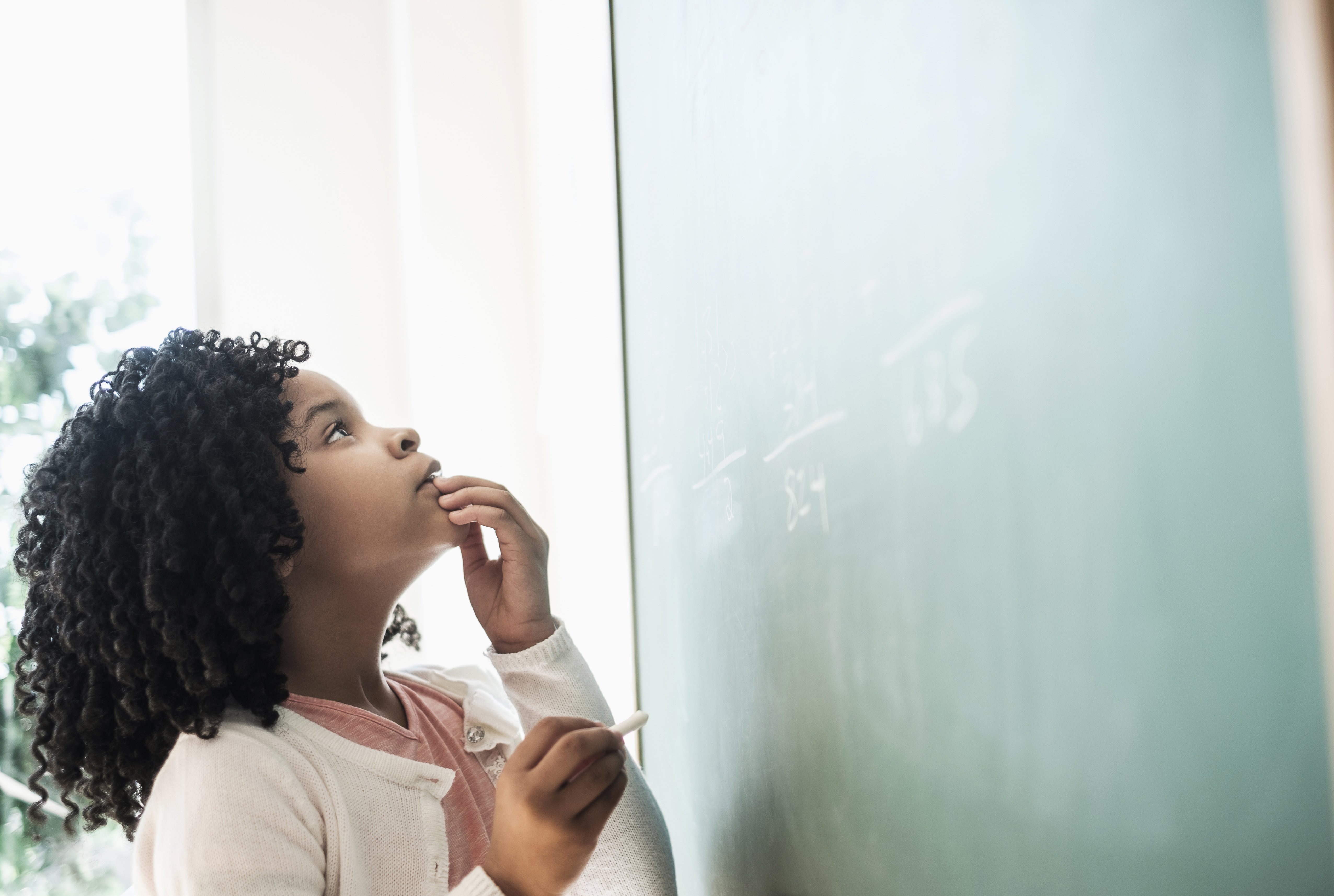 American student writing on chalkboard in classroom | Photo: Getty Images