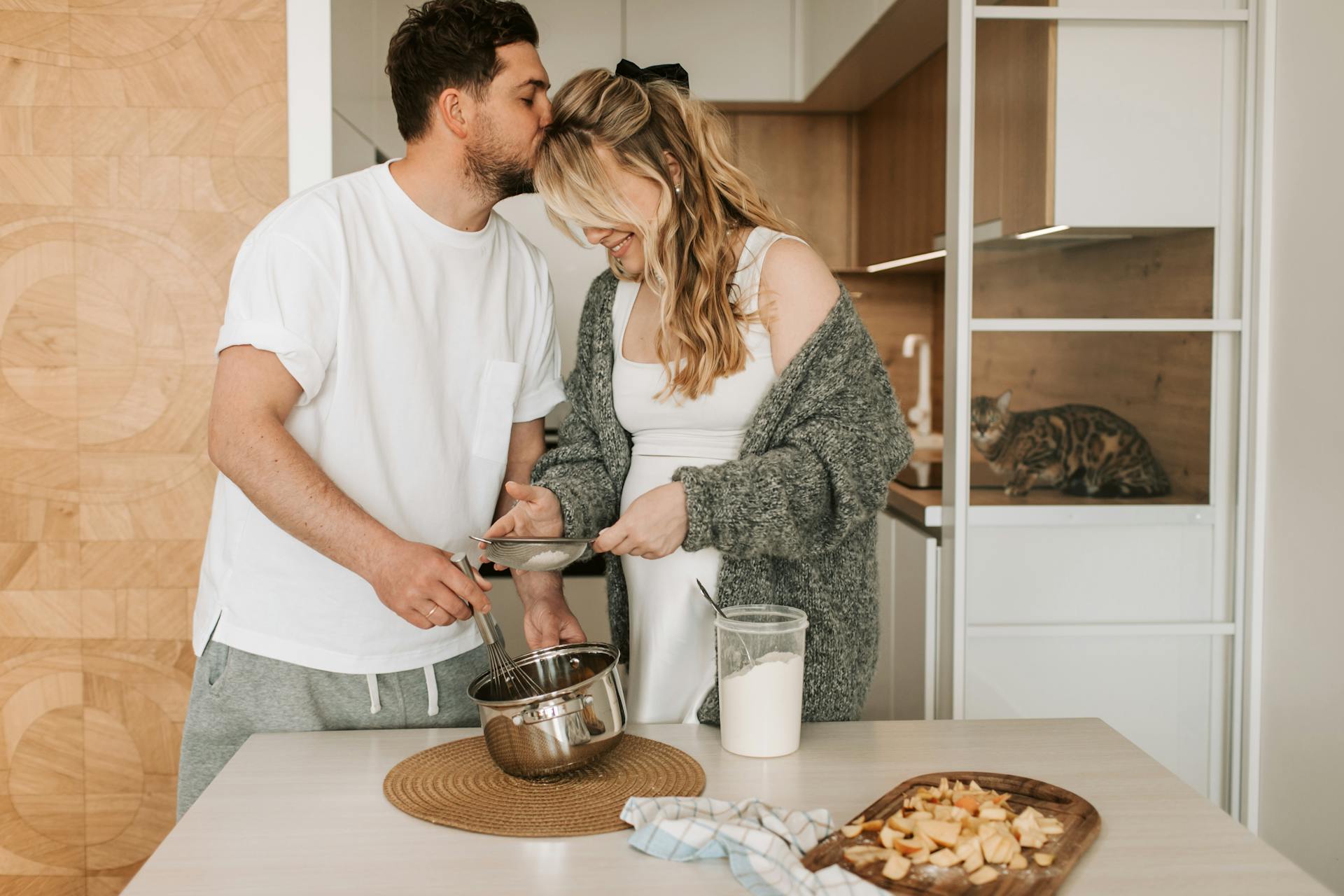 A husband kissing his pregnant wife's forehead while cooking | Source: Pexels