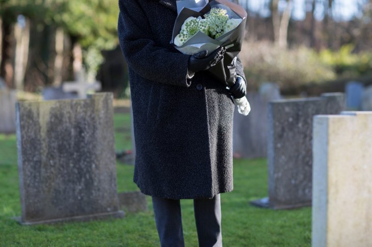 Une personne en deuil tenant un bouquet de fleurs dans un cimetière| Source : Shutterstock Une personne en deuil tenant un bouquet de fleurs dans un cimetière| Source : Shutterstock