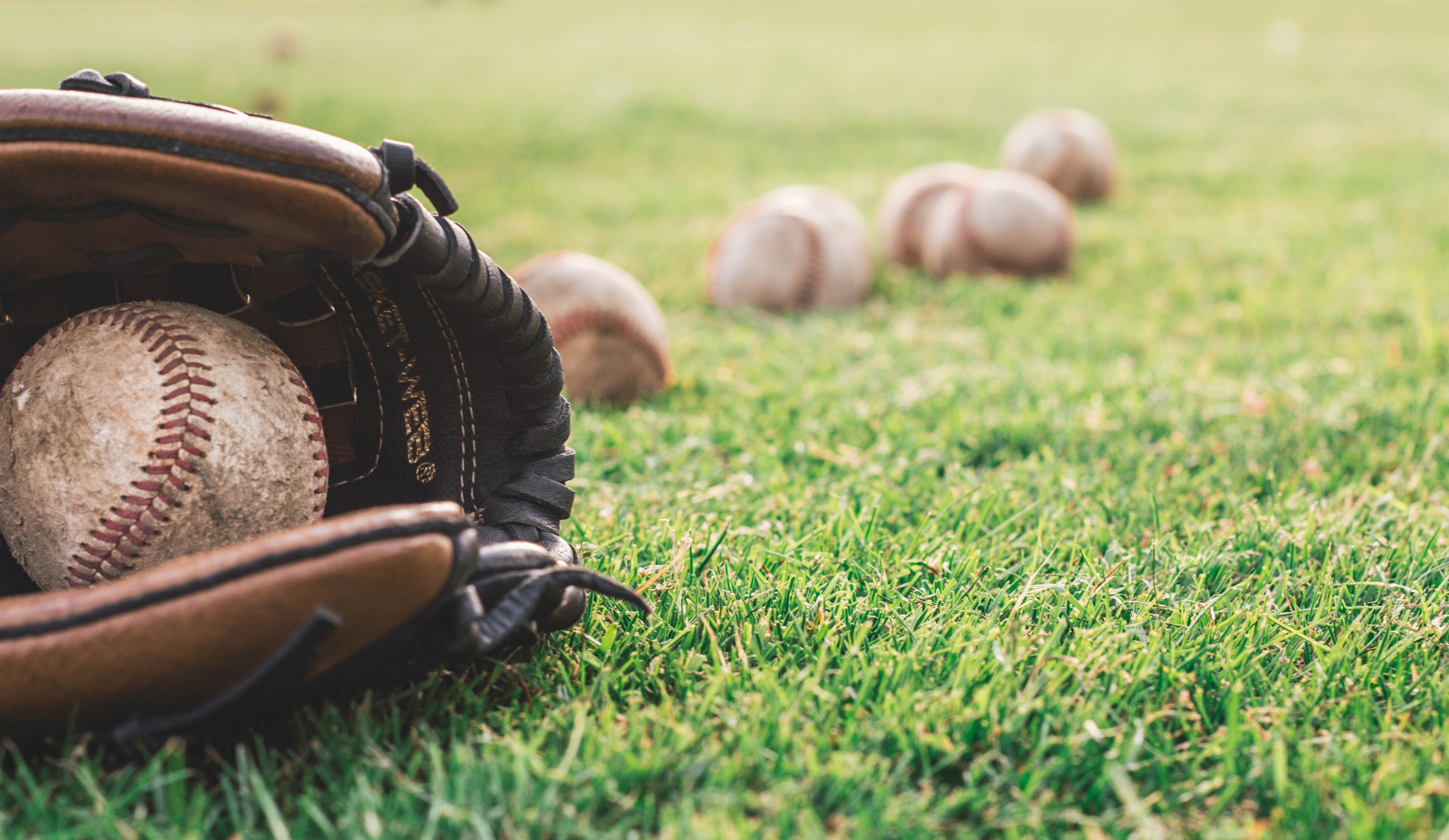 Baseball glove and balls on a field. | Source: Pexels/ Steshka Willems