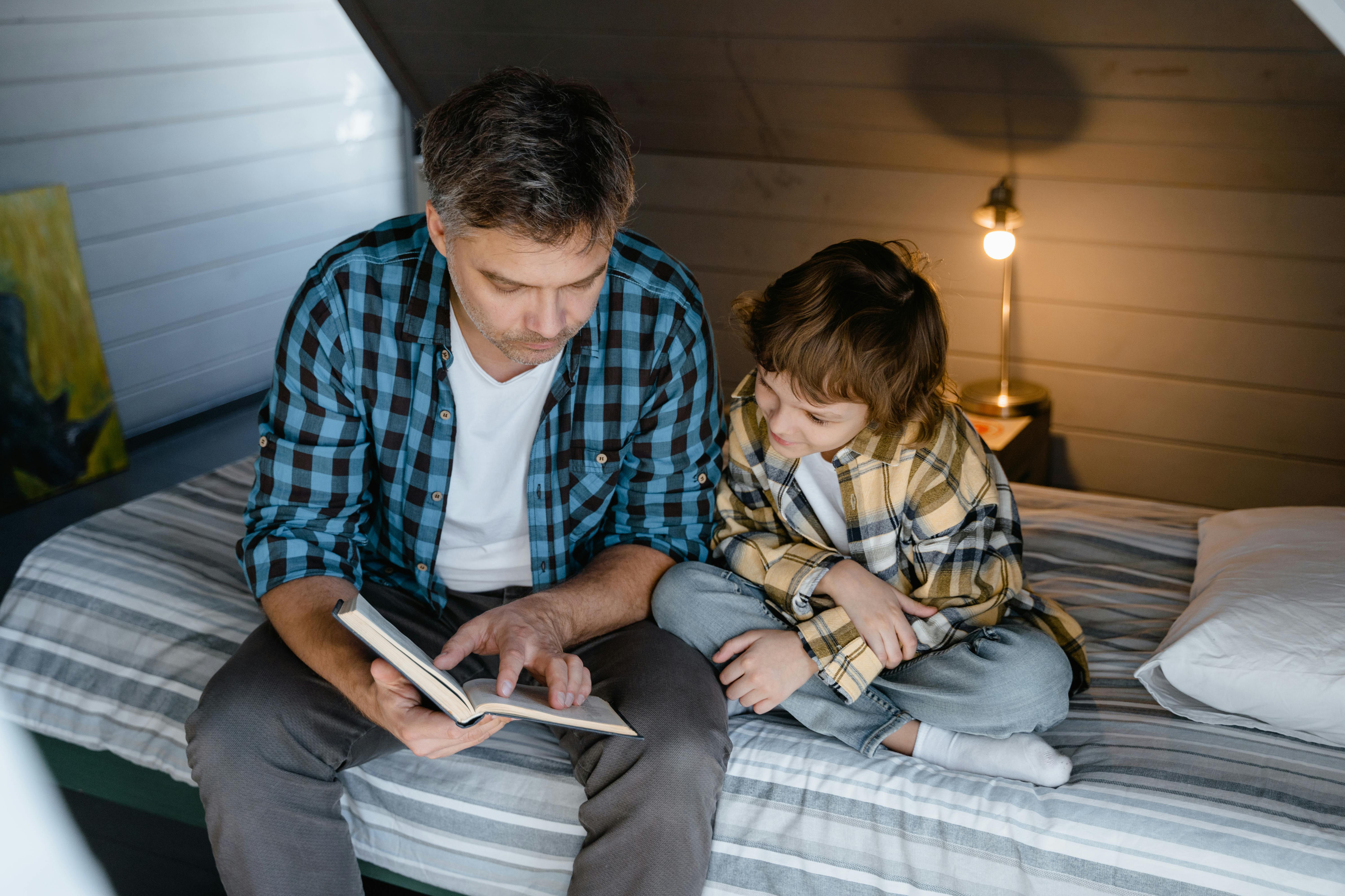 A man reads to a boy sitting together on a bed | Source: Pexels