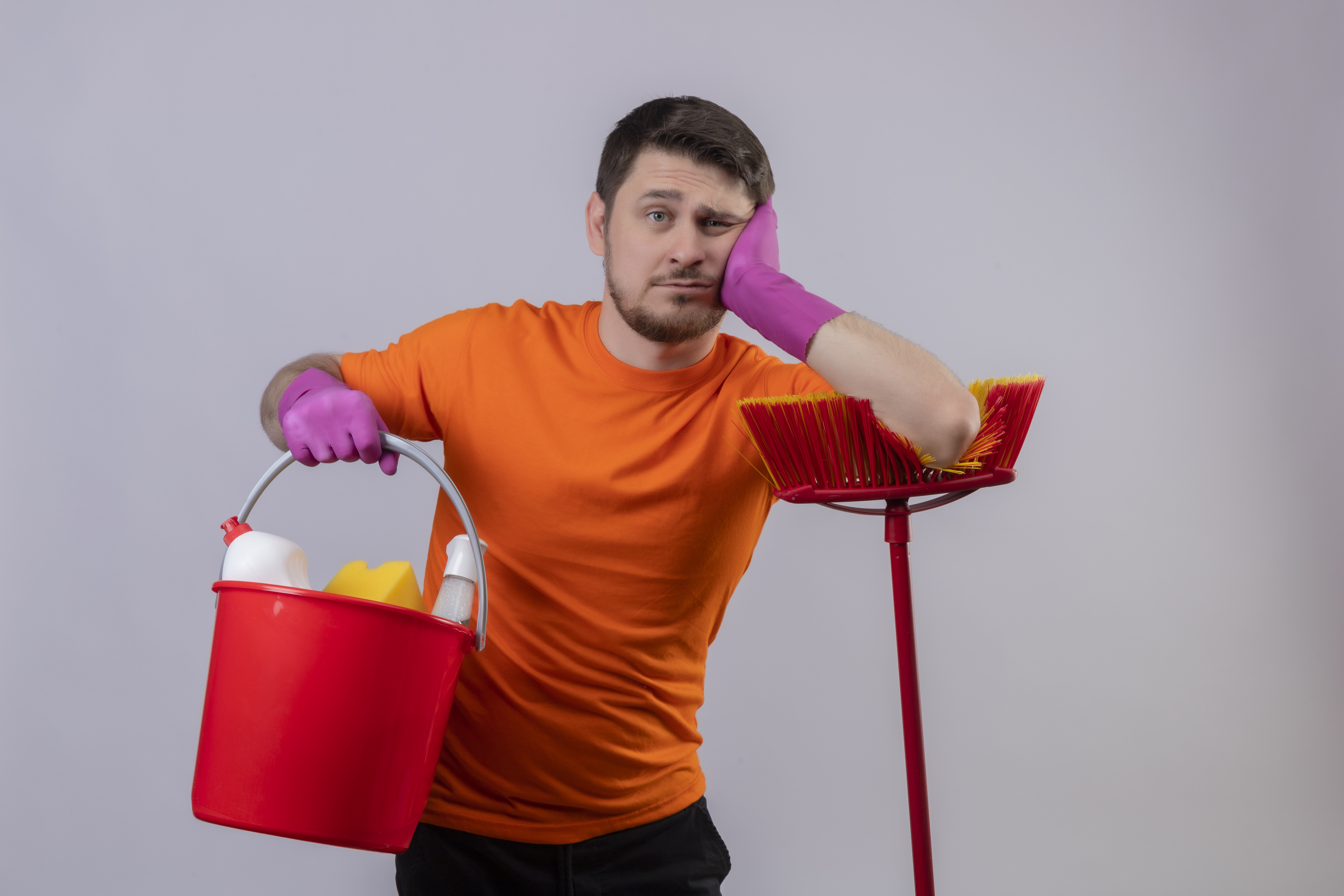 Young man in orange holding a bucket with cleaning tools and leaning on a mop | Source: stockking on Freepik