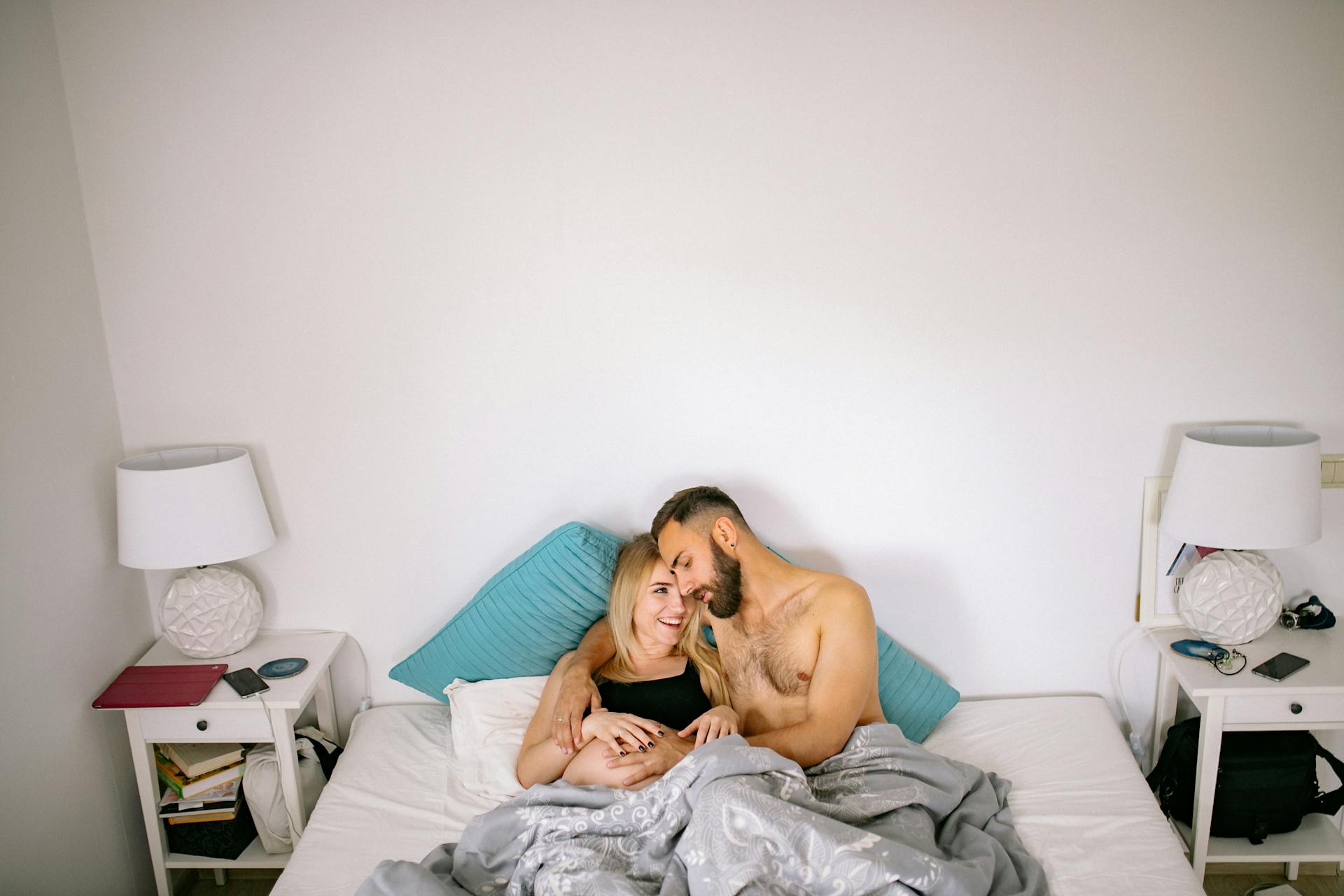 A husband touching his pregnant wife's baby bump while cuddling in bed | Source: Pexels