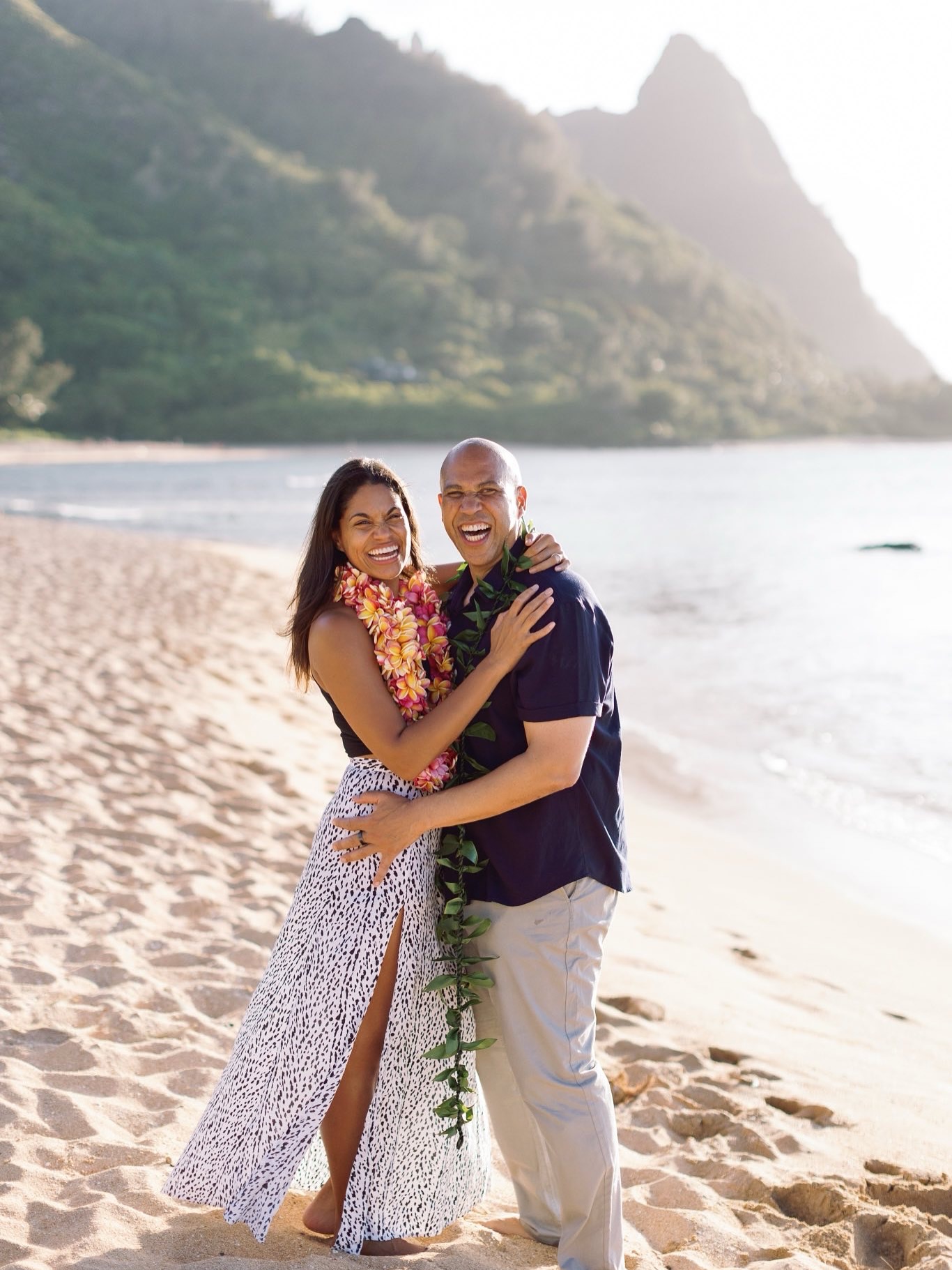 On a sunlit beach framed by green mountains, Cory Booker and Alexis Lewis smile wide, draped in vibrant leis. The couple stands barefoot in the sand, soaking in the moment with easy joy. | Source: Instagram/corybooker