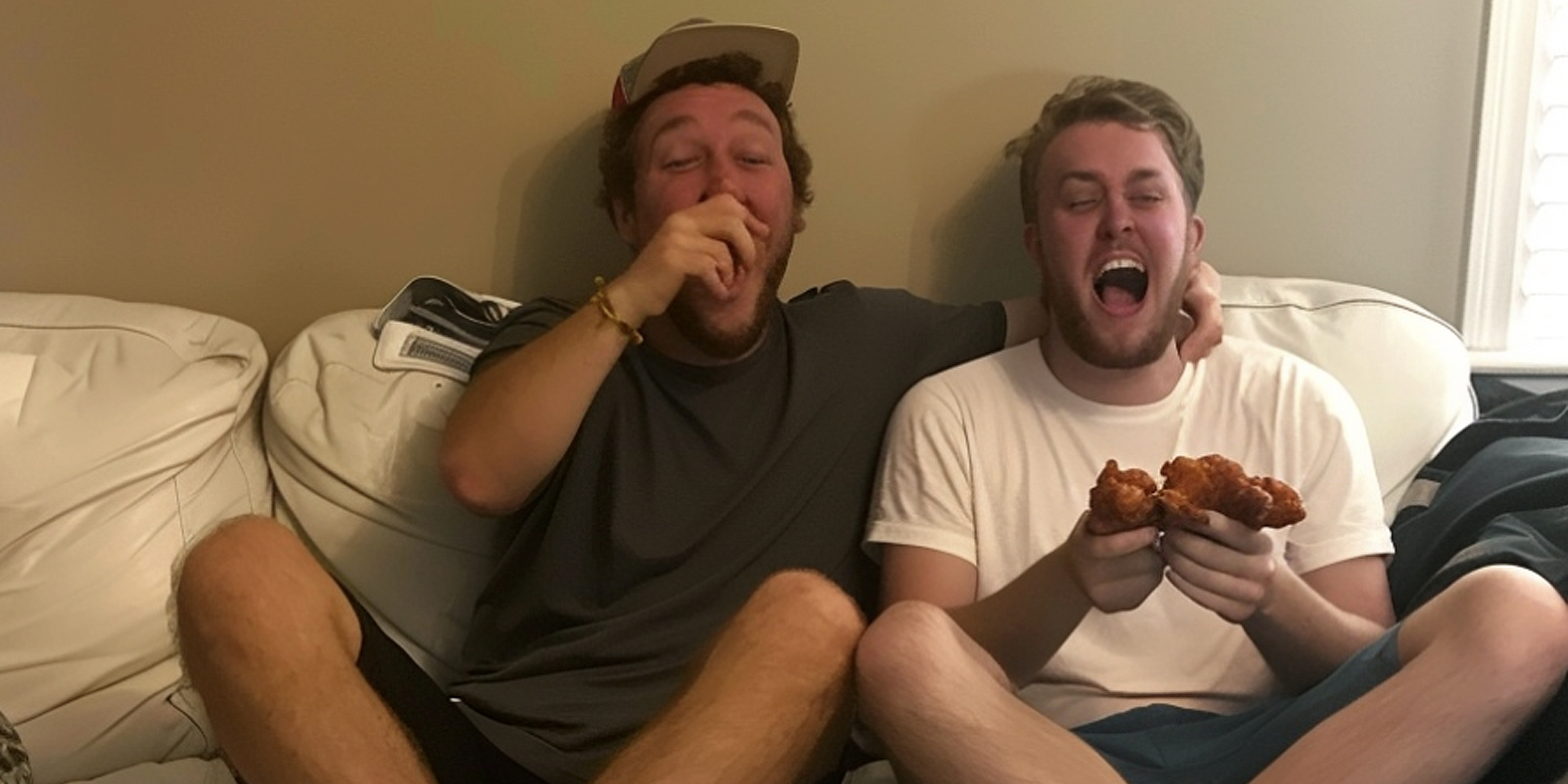 Two men eating and laughing on a couch | Source: AmoMama