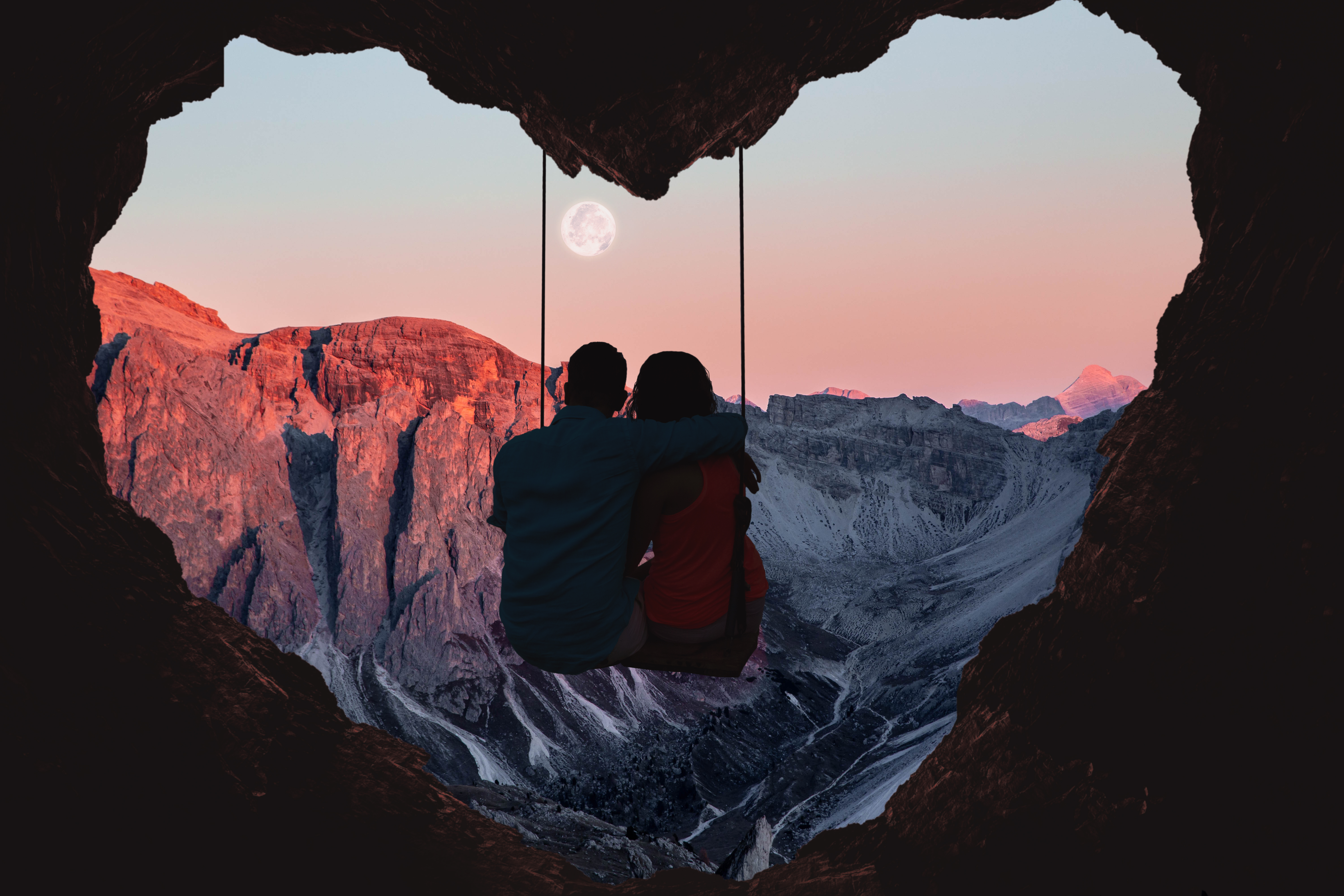 A couple sitting on a swing in heart-shaped cave, looking out at the Alps Mountains during sunset. | Source: Getty Images