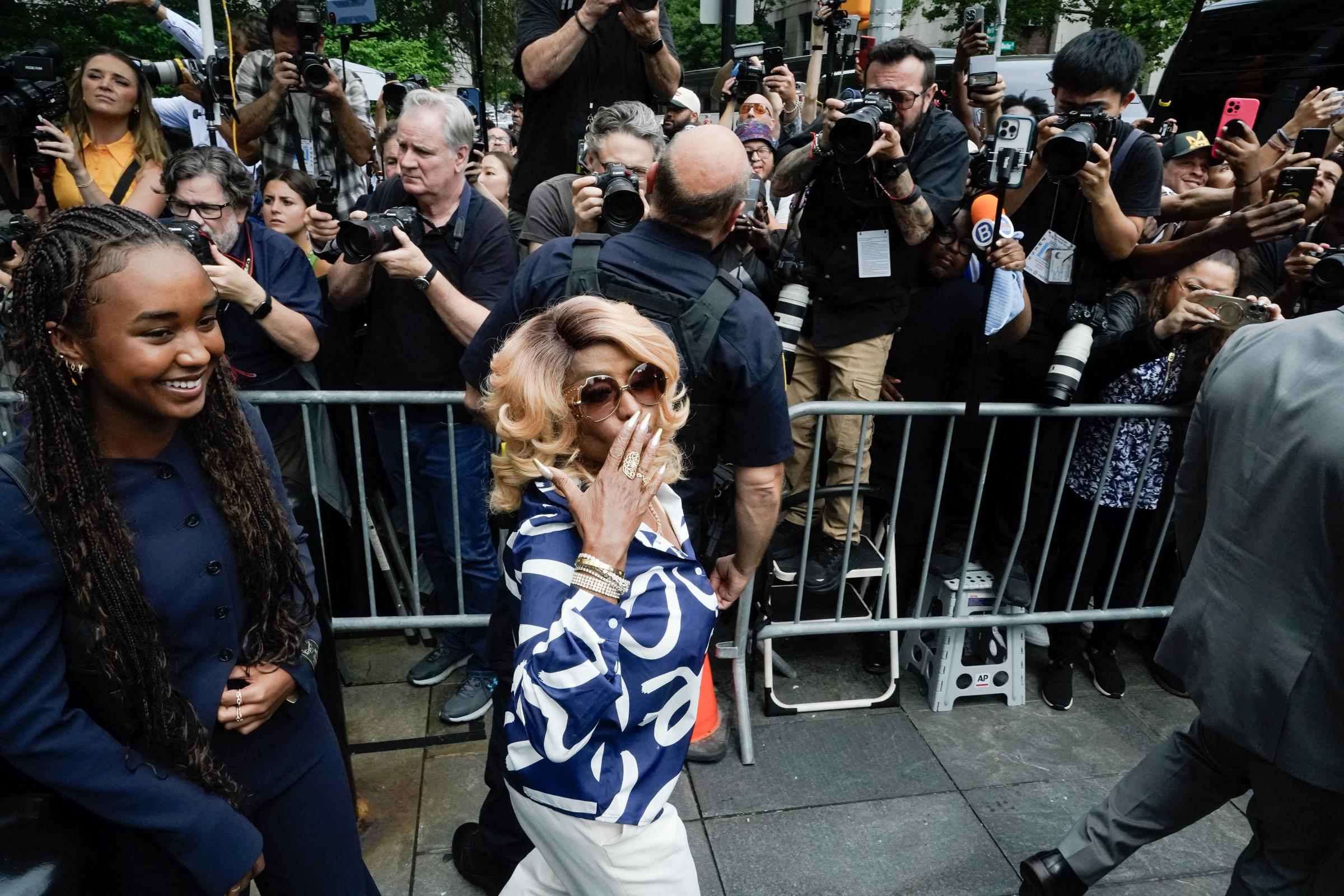 Janice Combs blows a kiss to a crowd of photographers while walking beside Chance Combs, who smiles brightly. The moment draws heavy media attention.