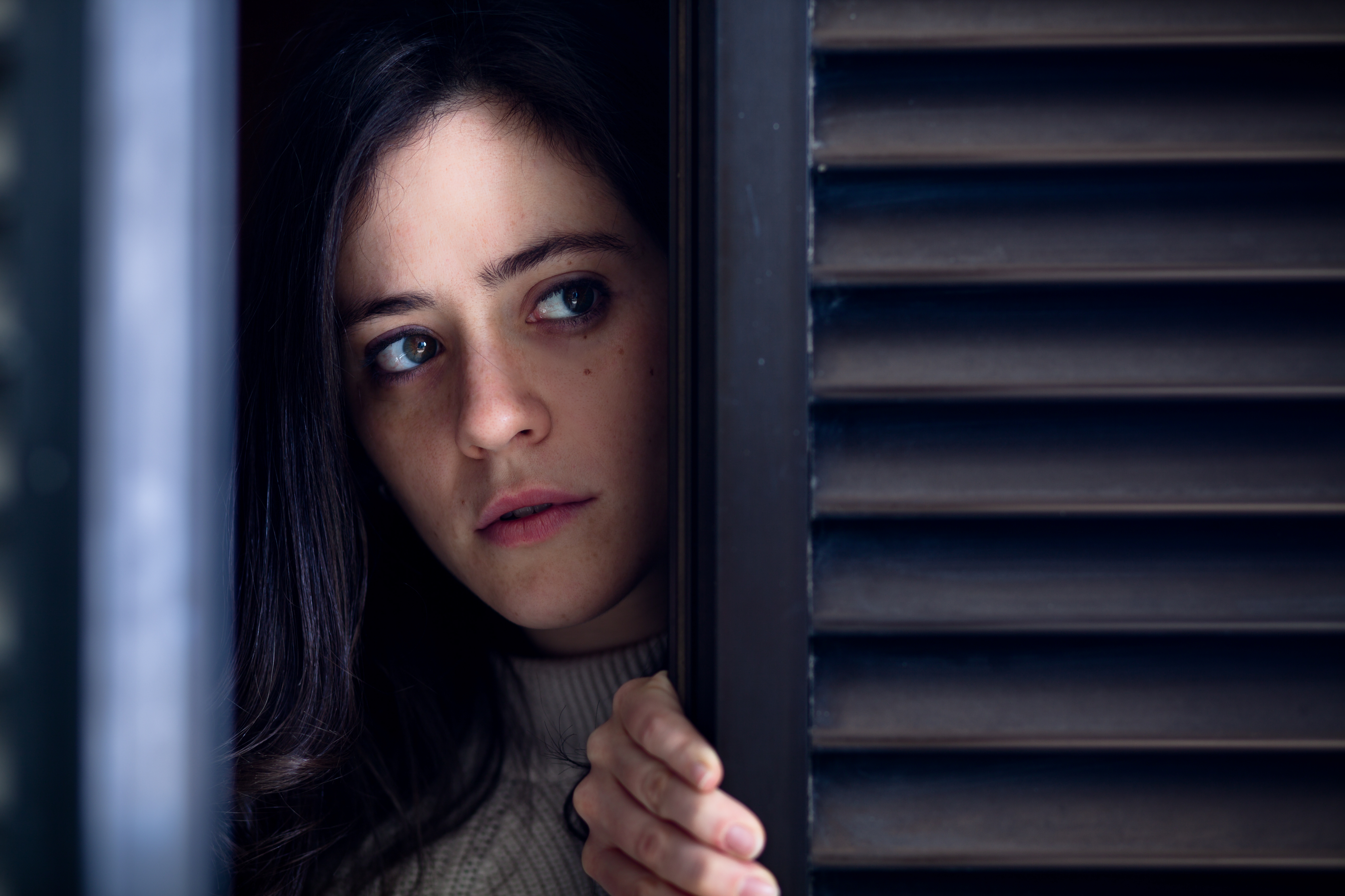 Worried Woman Watching Outside from a Wooden Window Shutter | Source: Shutterstock