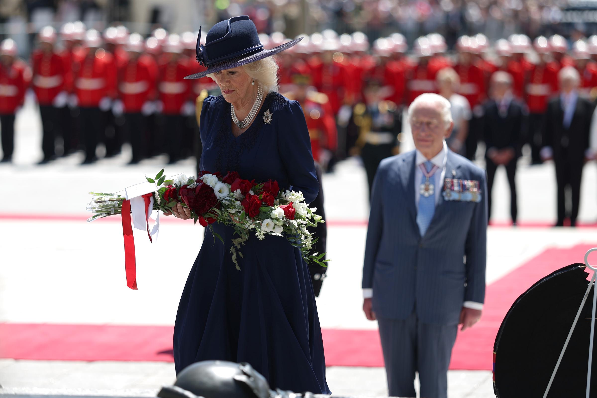 Queen Camilla holds a wreath as King Charles III looks on, with soldiers in the background, during a wreath-laying ceremony at the Tomb of the Unknown Soldier at the National War Memorial.