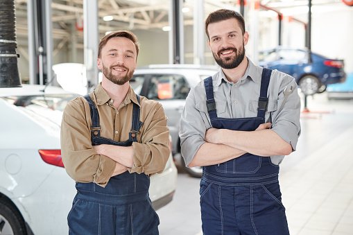 Photo of two bearded workers smiling at camera while posing in production workshop | Photo: Getty Images