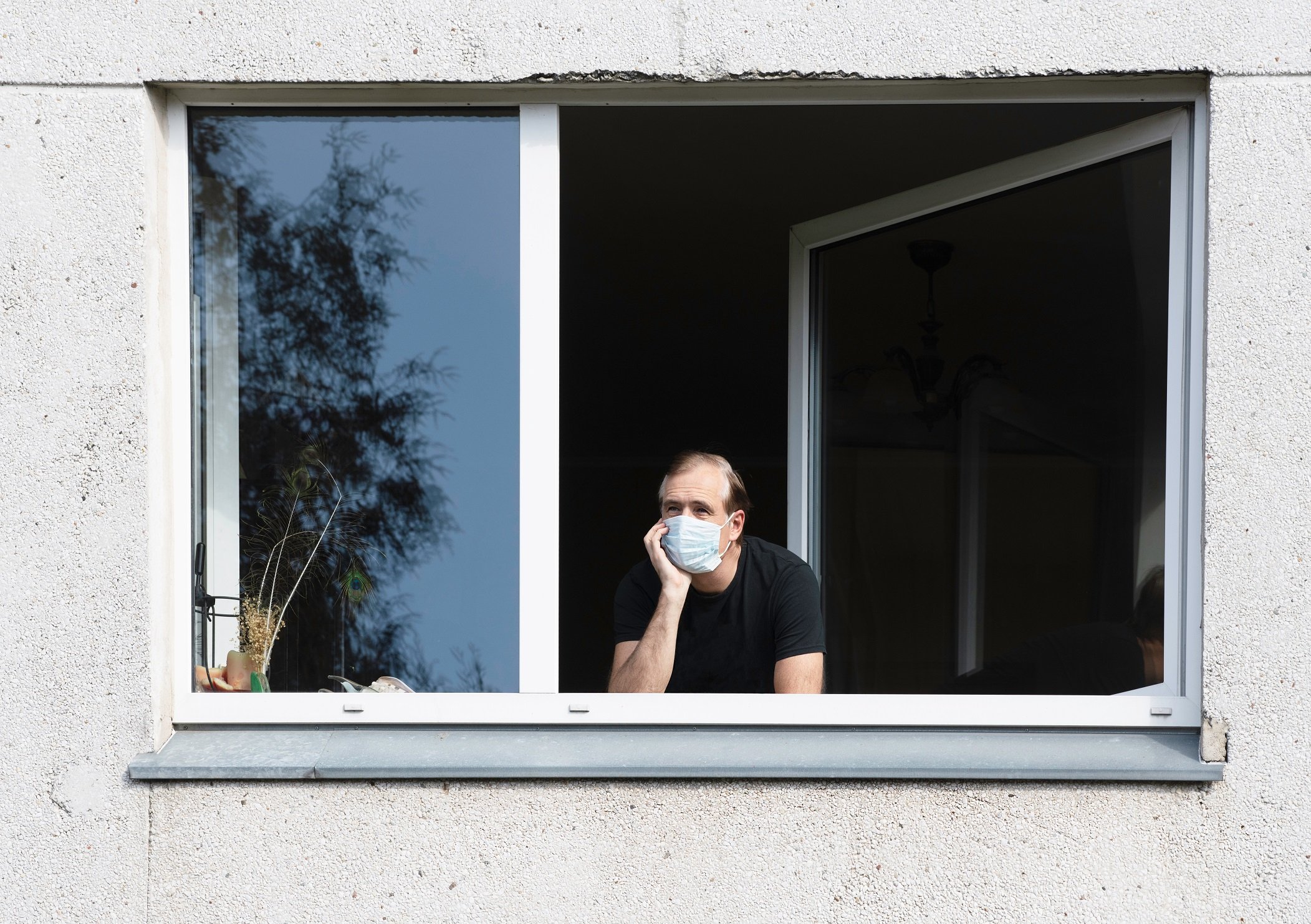 Hombre con mascarilla mira por la ventana durante el confinamiento. | Foto: Shutterstock