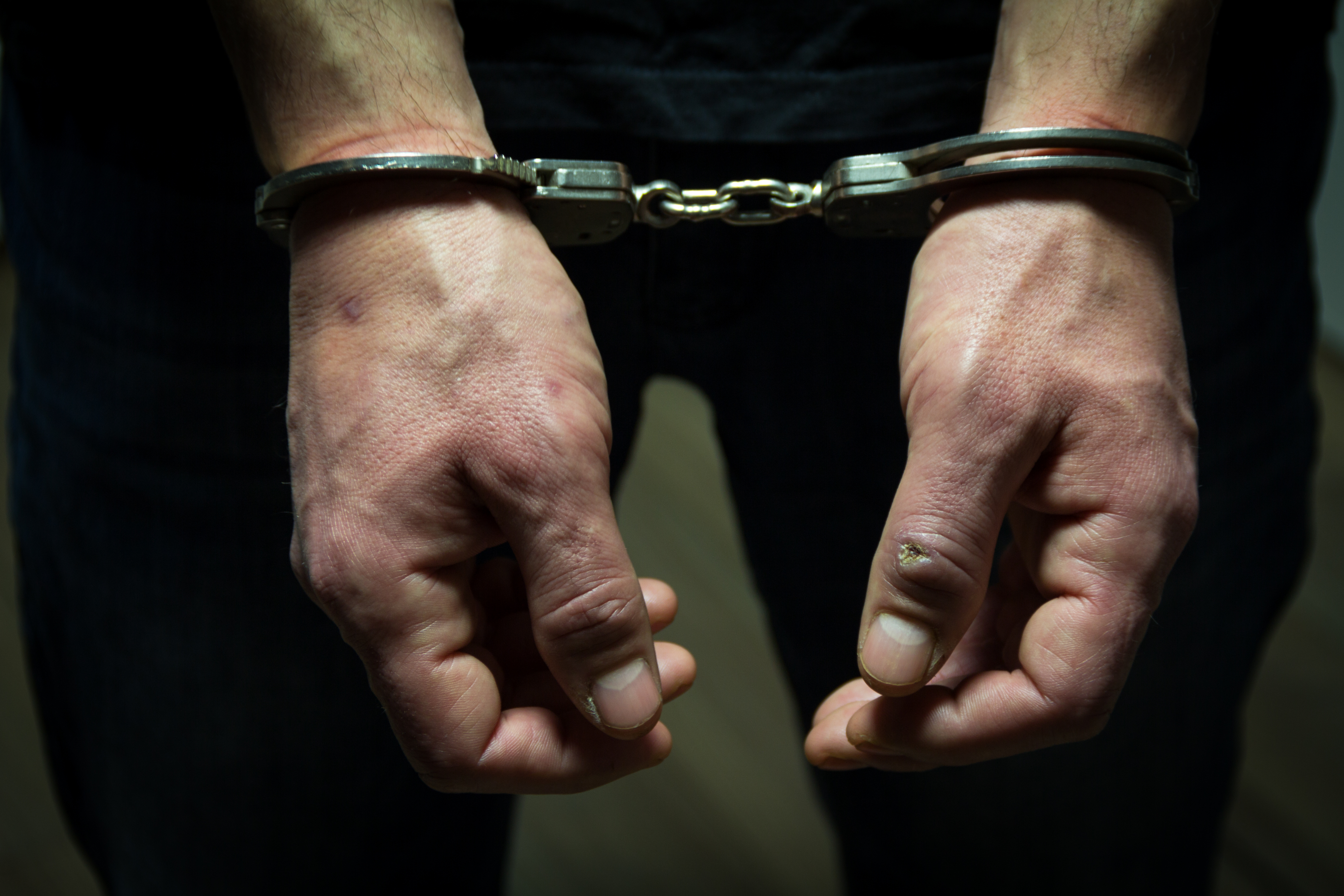 The arrested criminal handcuffed. Hands with handcuffs in the front | Source: Shutterstock