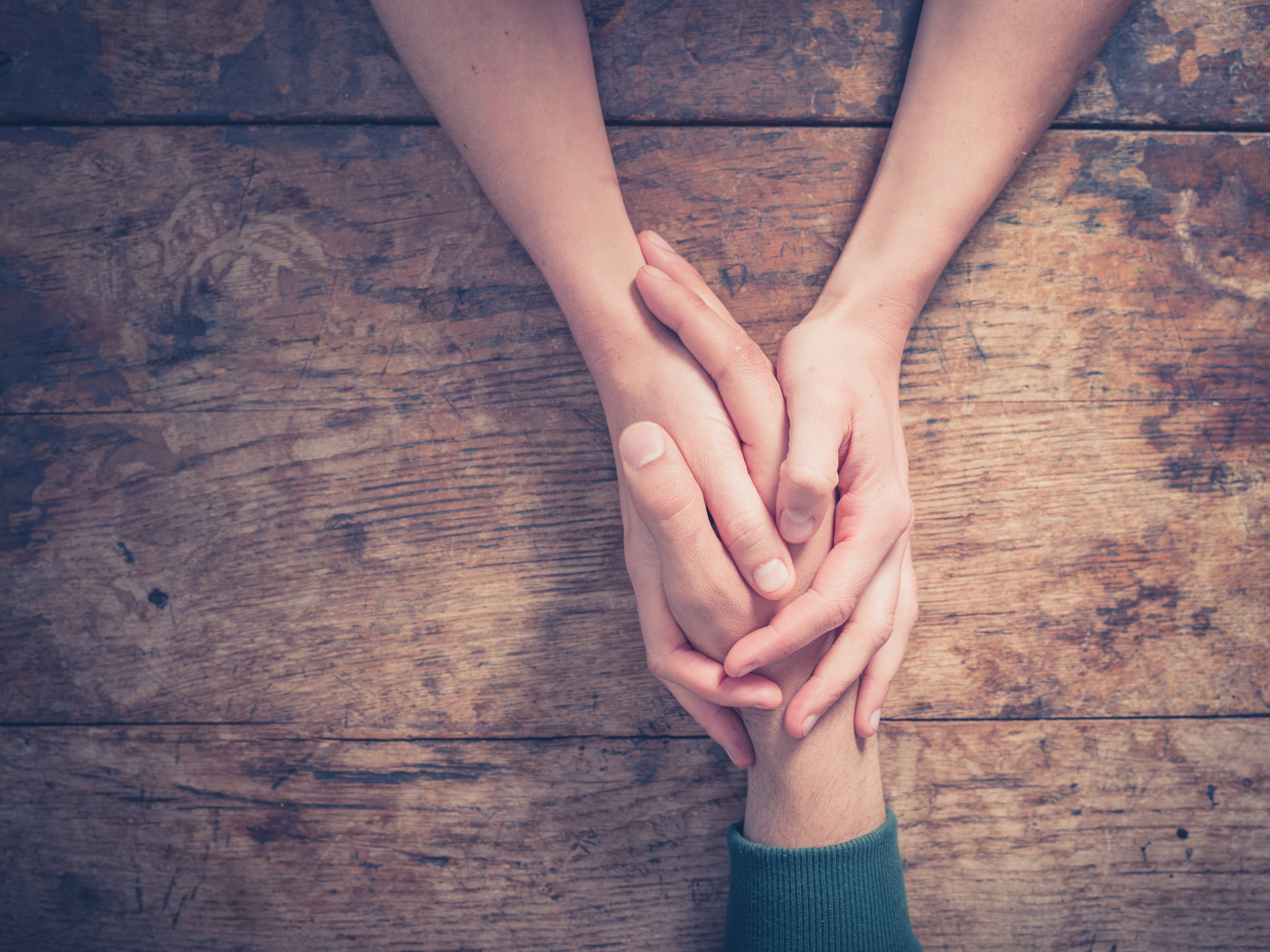 Close up on a man and a woman holding hands at a wooden table. | Source: Shutterstock