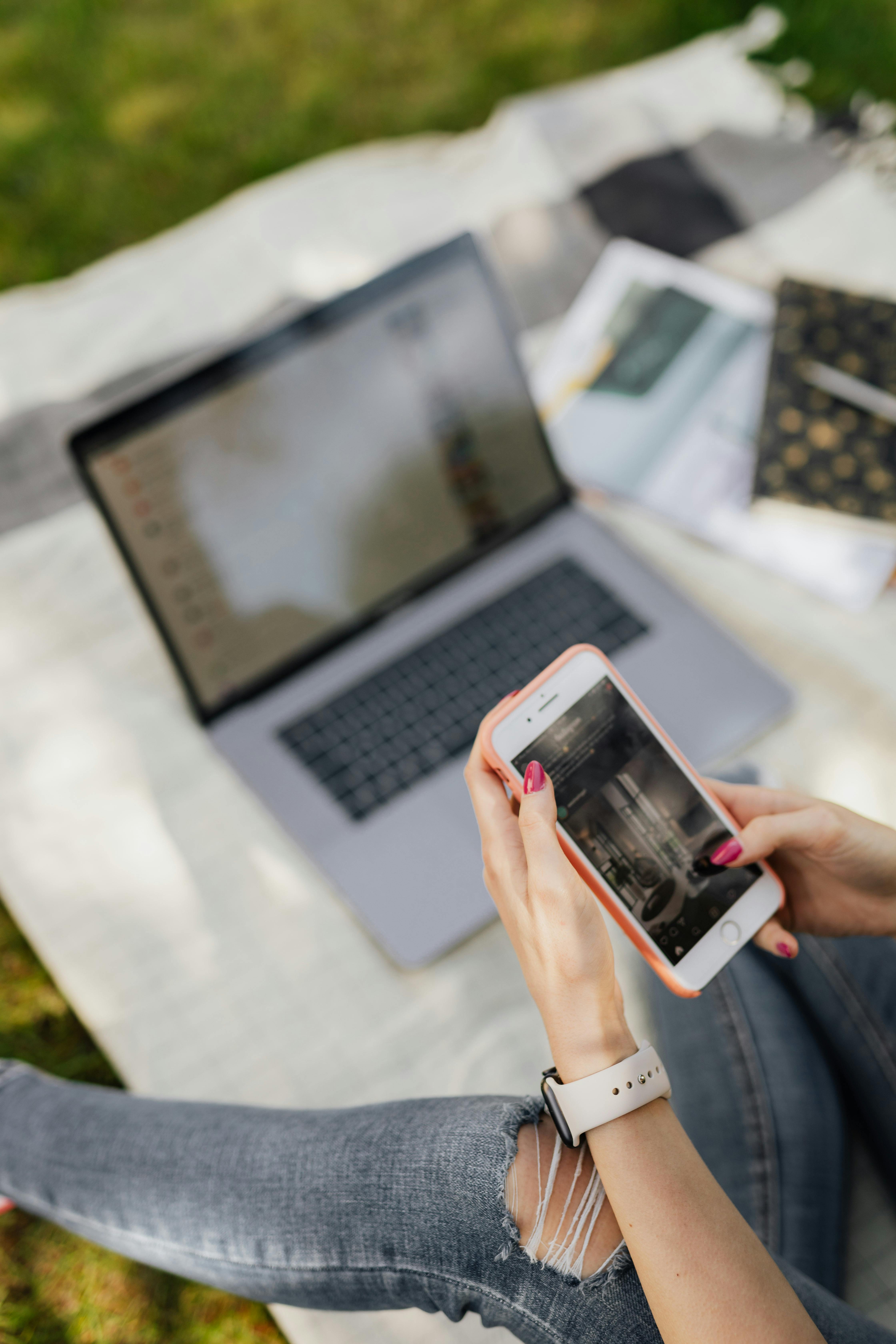 A woman using a phone with an open laptop in the background | Source: Pexels