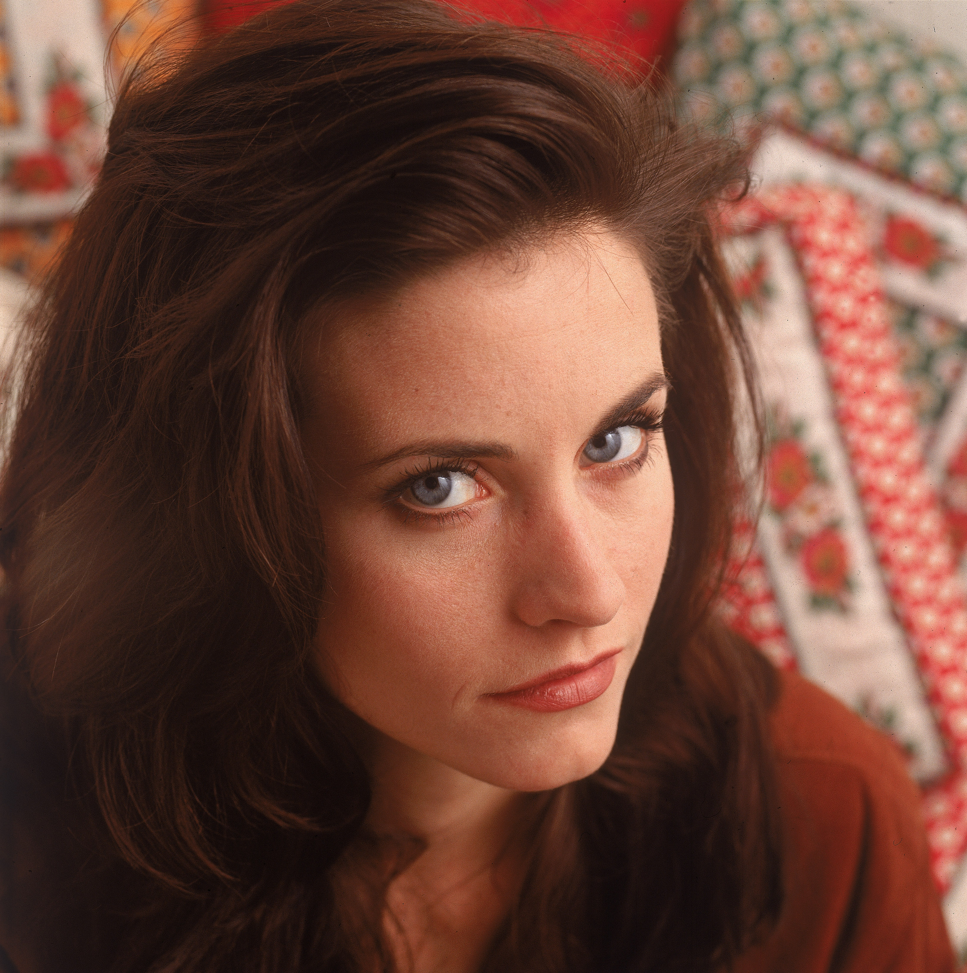 Courteney Cox stuns in a 1990 close-up, highlighting her striking blue eyes, bold red lipstick, and gold dangling earrings, all paired with a stylish green suit.