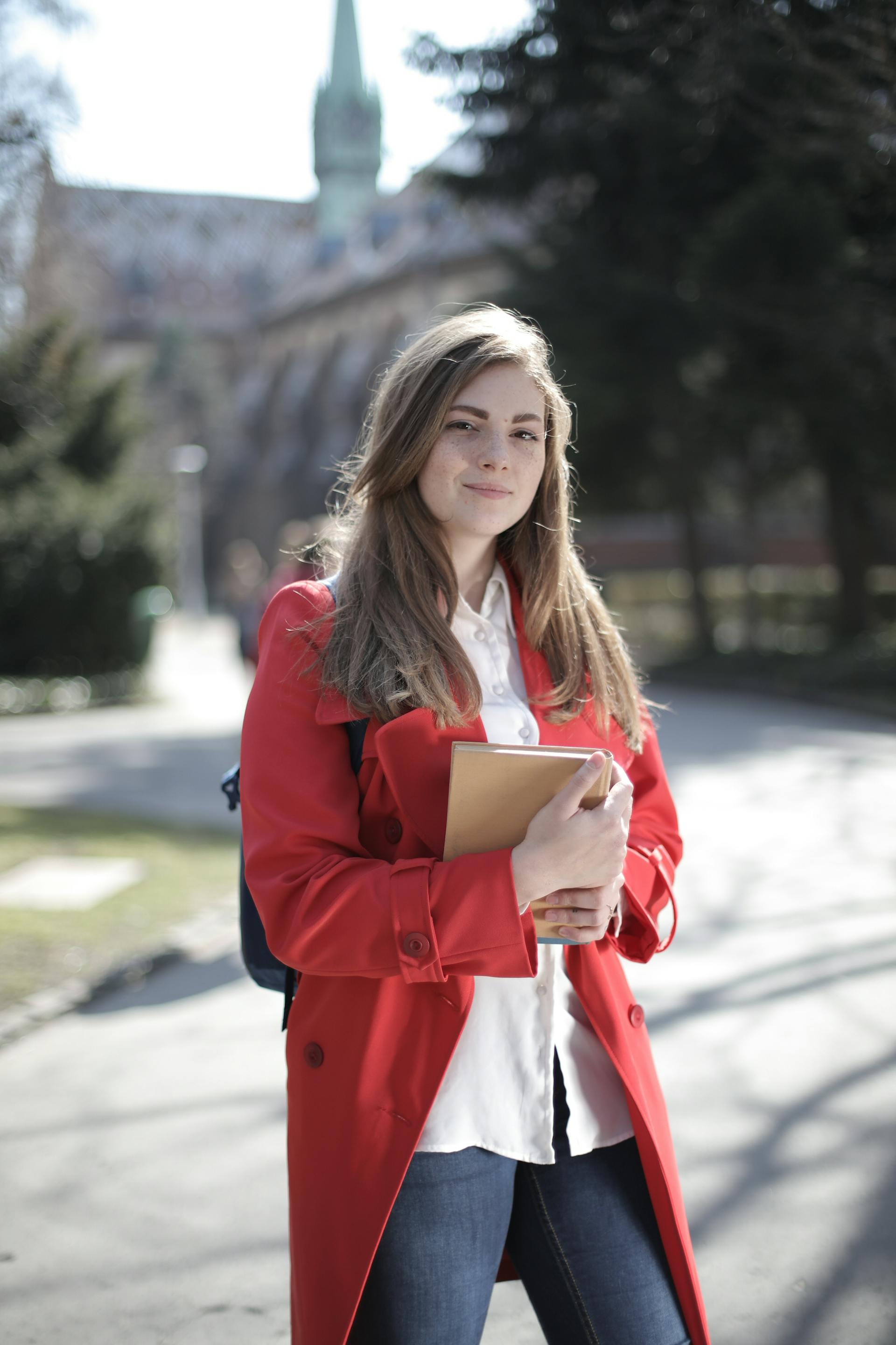 A woman in a red coat carrying a backpack and a brown book | Source: Pexels