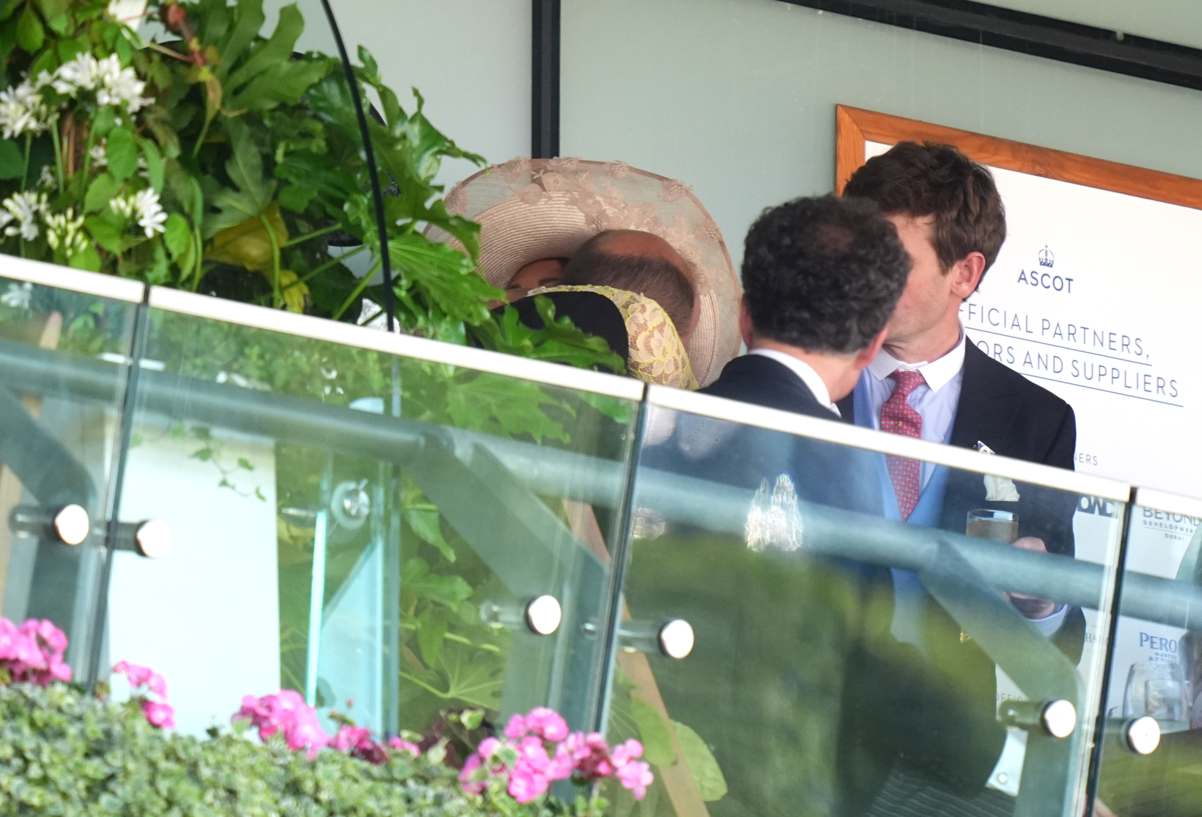 Prince William and Carole Middleton share a warm embrace in a rare public display of affection, partially hidden behind her wide-brimmed hat, as onlookers mingle nearby in the royal box.