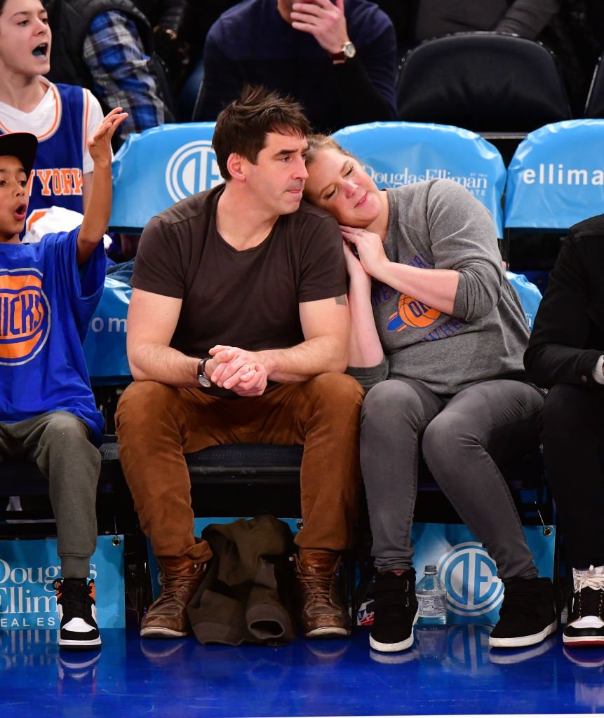 Amy Schumer leans on her husband Chris Fischer's shoulder while watching a basketball game for the Washington Wizards versus New York Knicks game, at Madison Square Garden on December 23, 2019, New York | Source: James Devaney/Getty Images